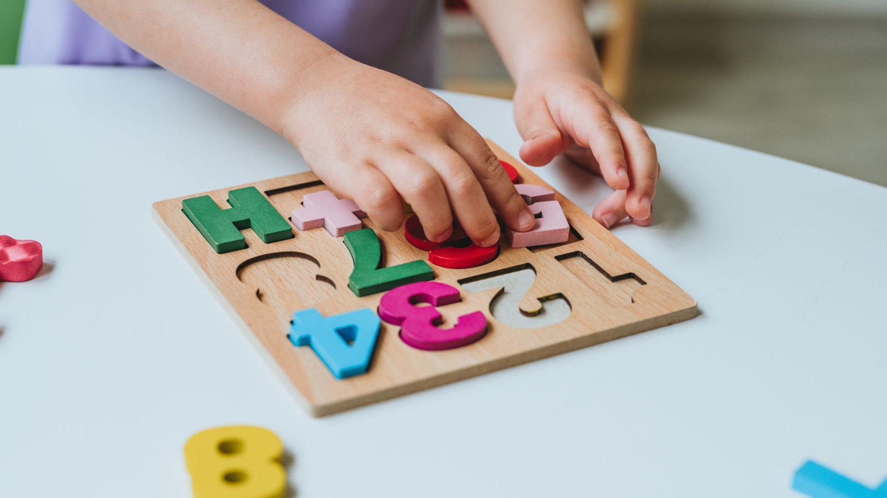 Close-up of little girl's hands playing with colorful numbers puzzle standing in the classroom in kindergarten