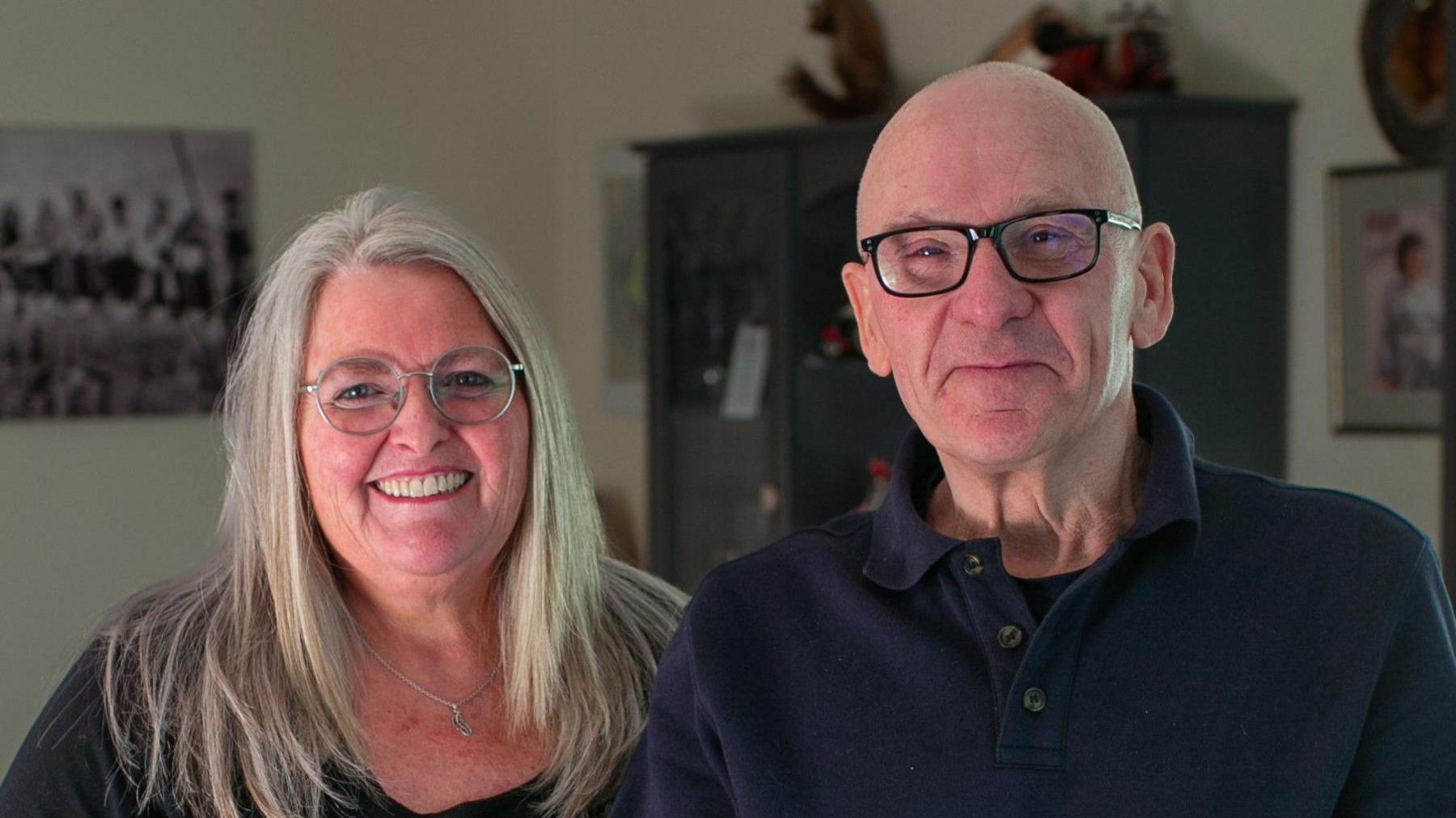 Miriam Doyle and Paul Perkins. Miriam has long blonde hair and glasses, and Paul is tall, bald and has glasses.