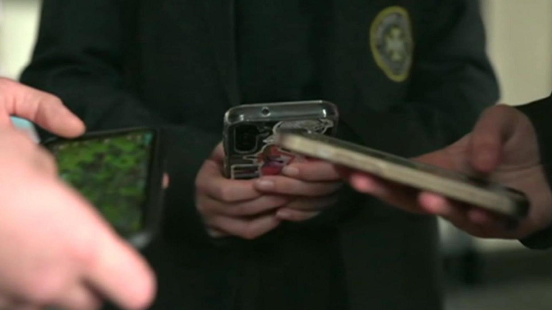 A close up view of phones being held and used by three school pupils.