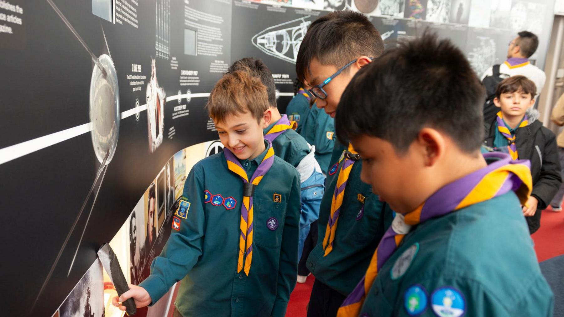 Three scouts looking at a wall display 