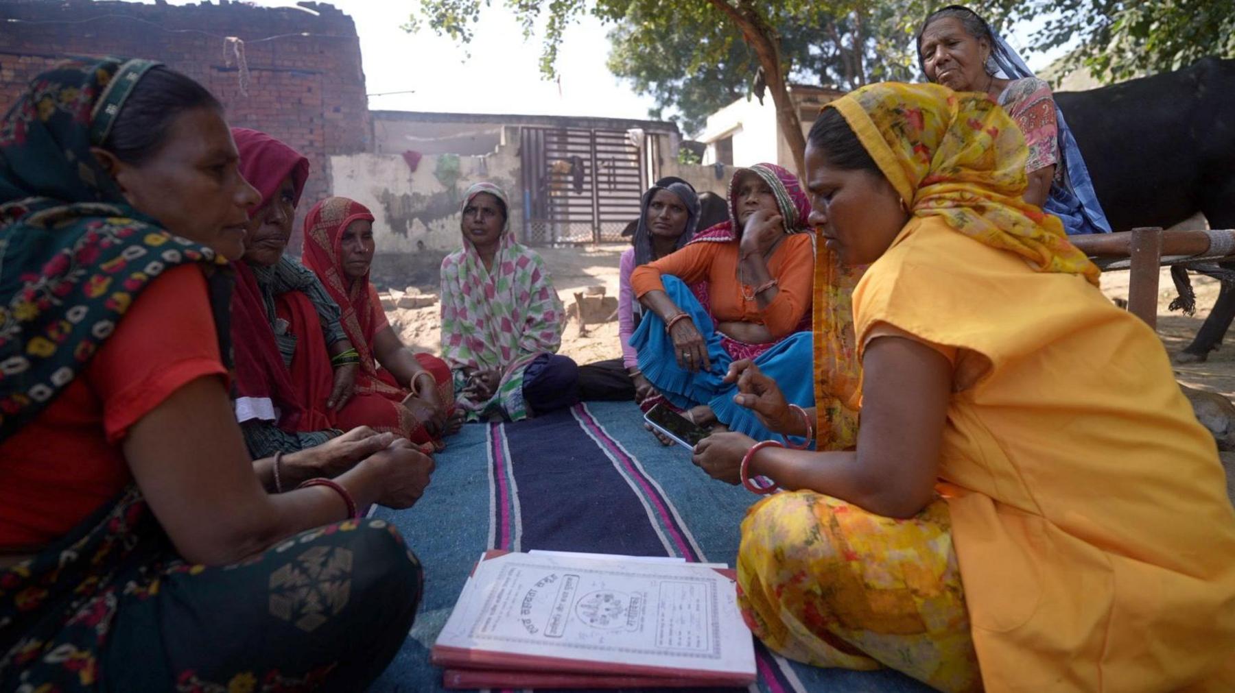 A group of women sitting together on the ground as one of them uses her phone in India's Haryana state