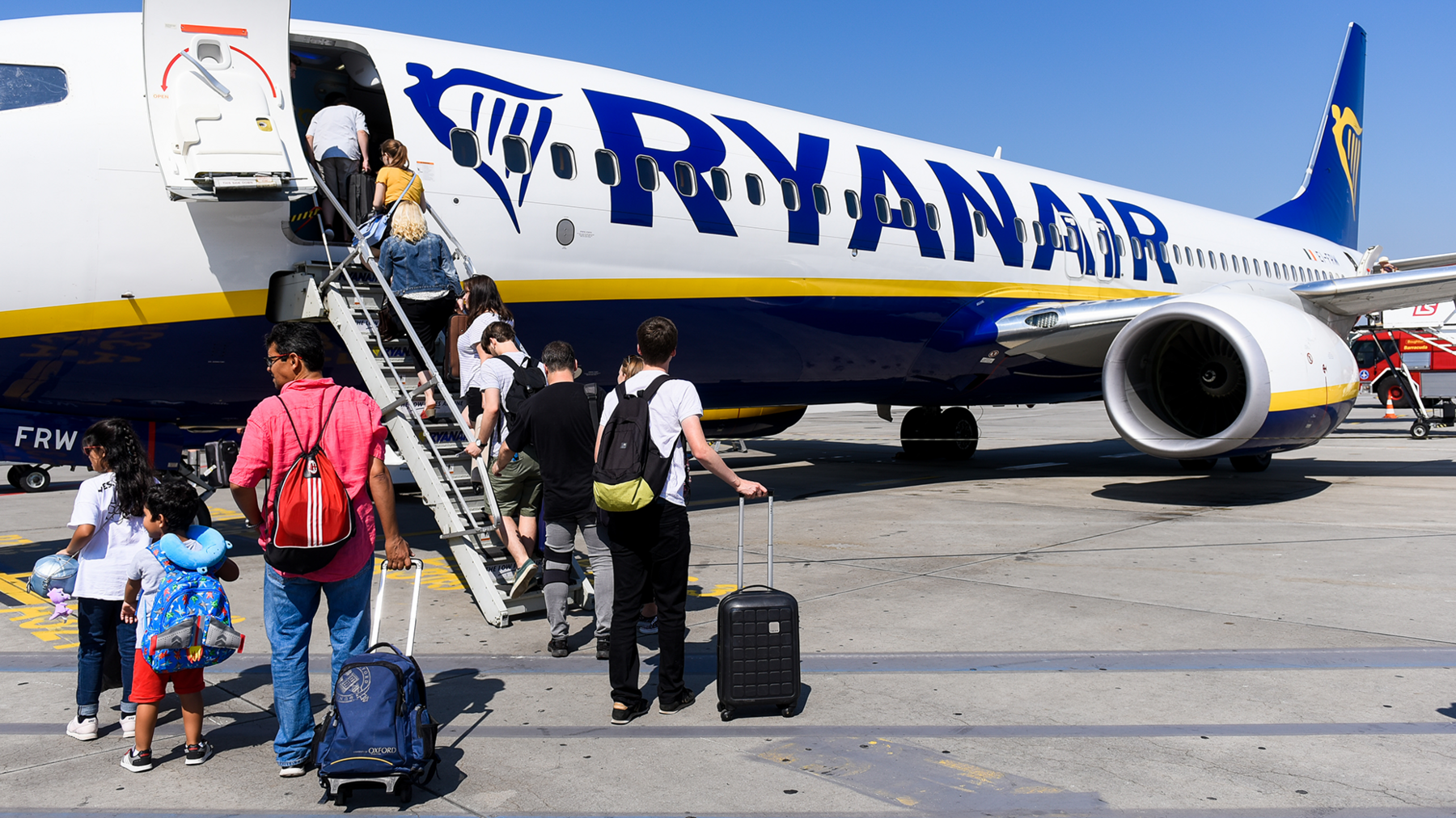 Passengers including children boarding a Ryanair aircraft on the steps at the fron of the plane on a sunny day with blue skies