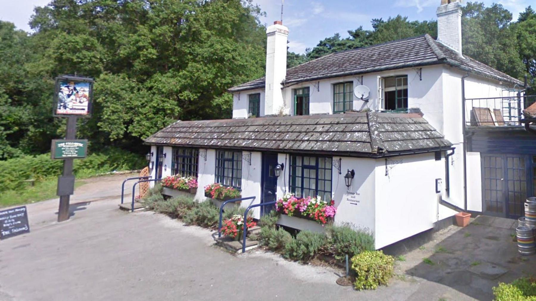 A white pub with two chimneys and dark grey tiles. 