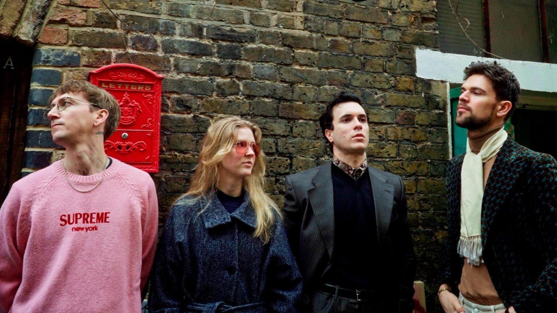 A band photo of The Great Leslie, which is made up for four musicians who, in this image, are standing in front of a brick wall