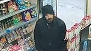 A CCTV image of William Riddell wearing a black jacket and black hat, walking into a newsagents. He can be seen between two aisles filled with sweets. 