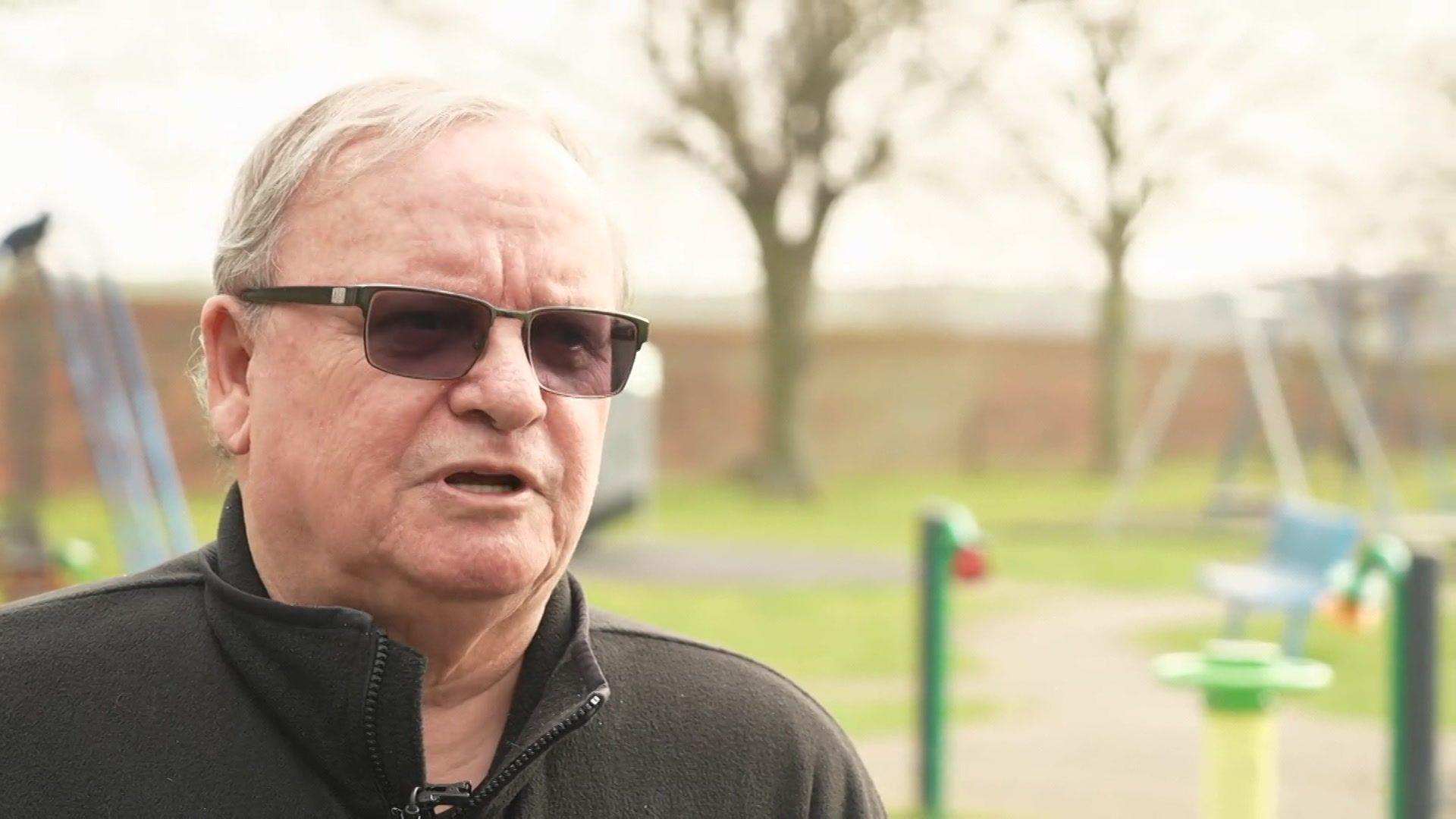 An elderly man stands next to a playground