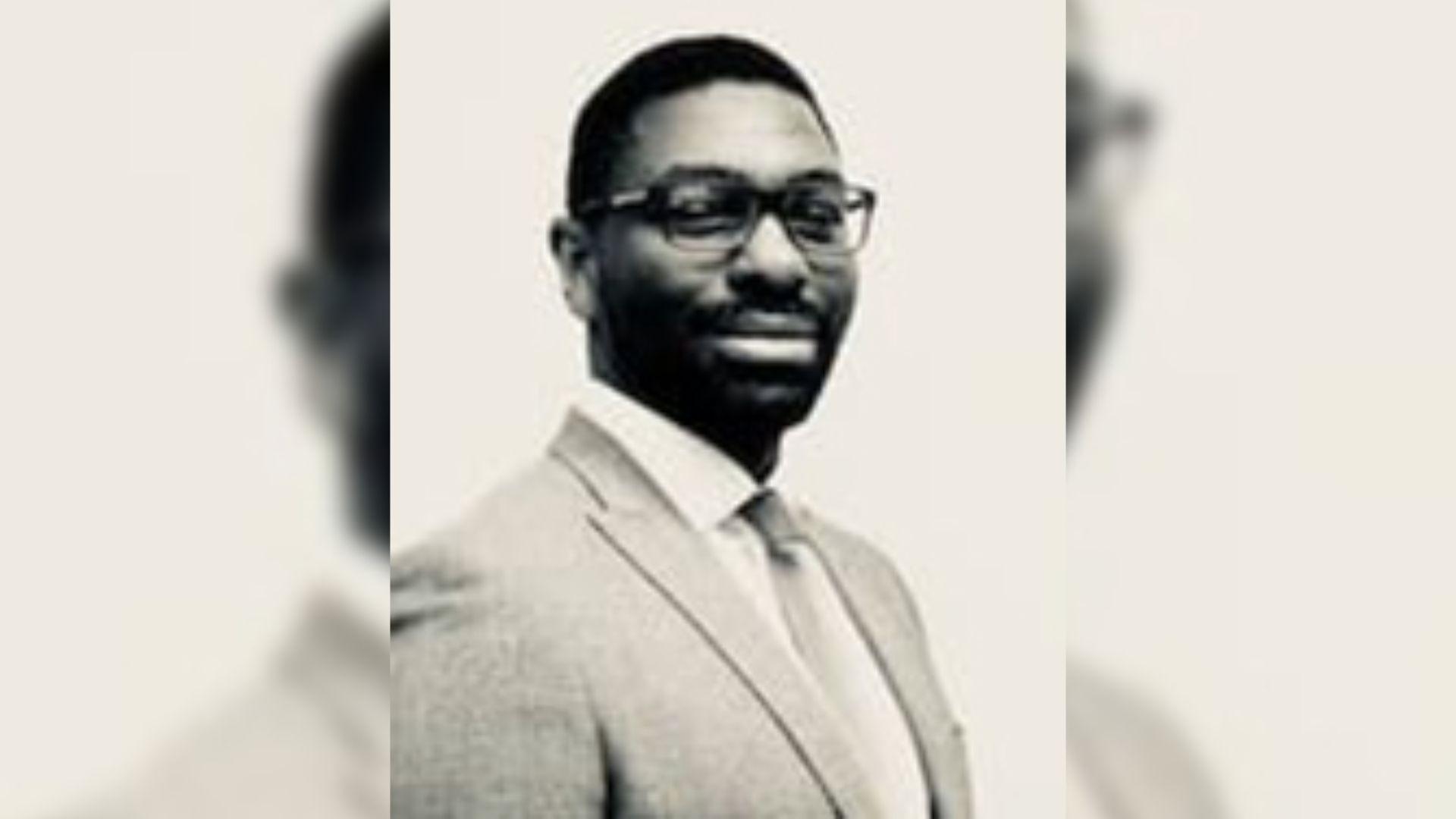 A sepia image of Damo Awobajo, a man wearing glasses, a suit jacket plus a shirt and tie.