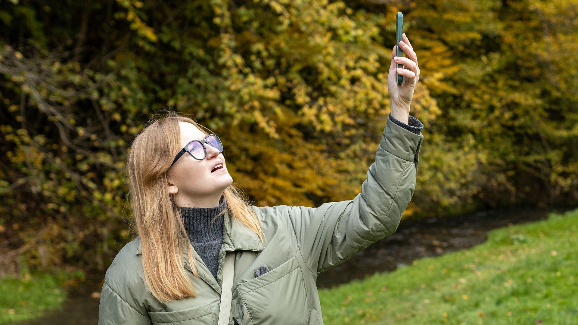 A young woman in the countryside holding up her mobile phone  to try and get better phone signal