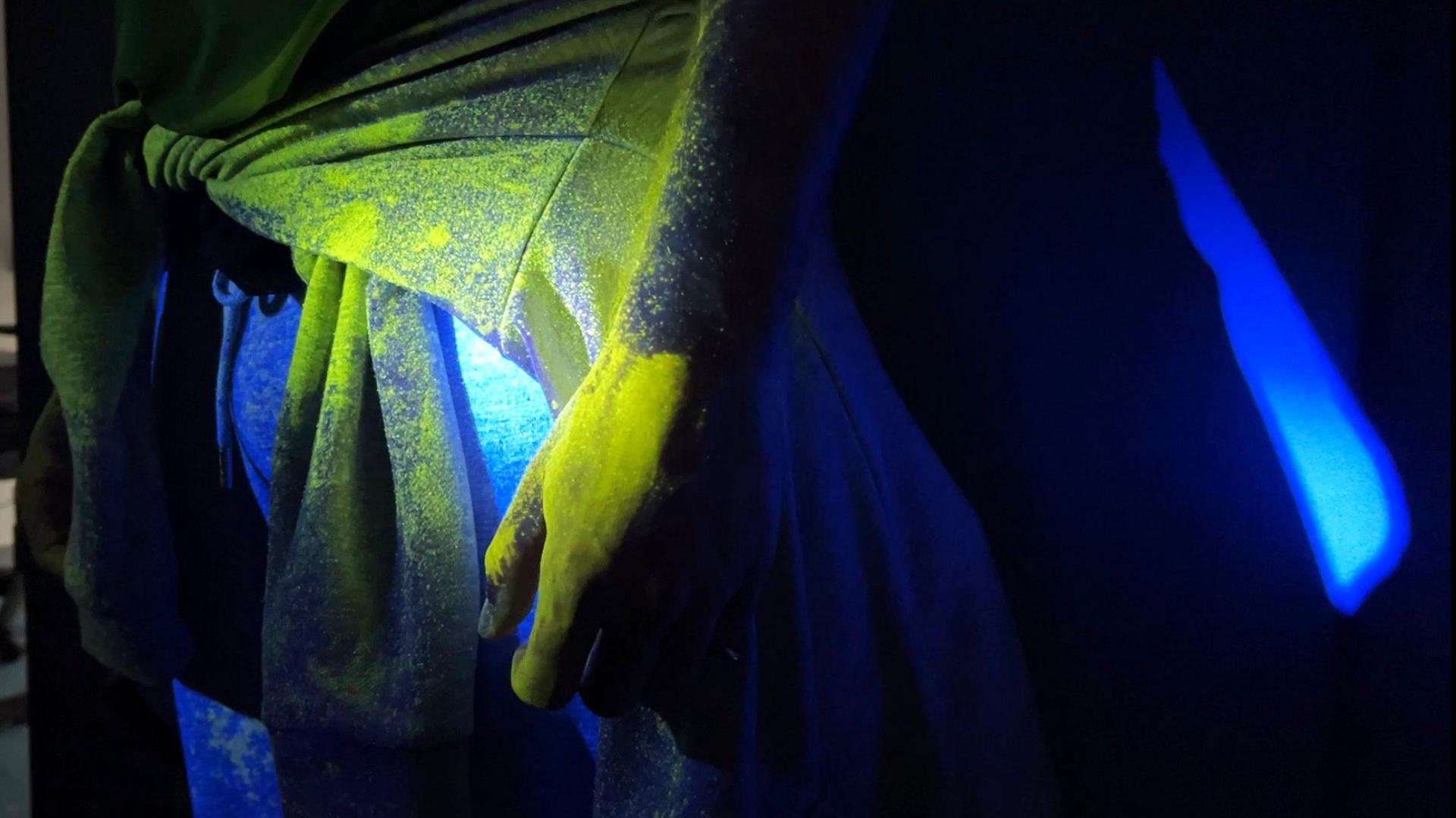 Close-up of a hand and a shirt showing the Smartwater spray glowing yellow under ultraviolet light