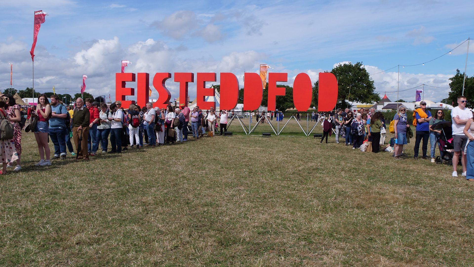 Roedd y ciw i'r Pafiliwn ar gyfer y gystadleuaeth Côr newydd i'r Eisteddfod yn cyrraedd yr arwydd mawr coch