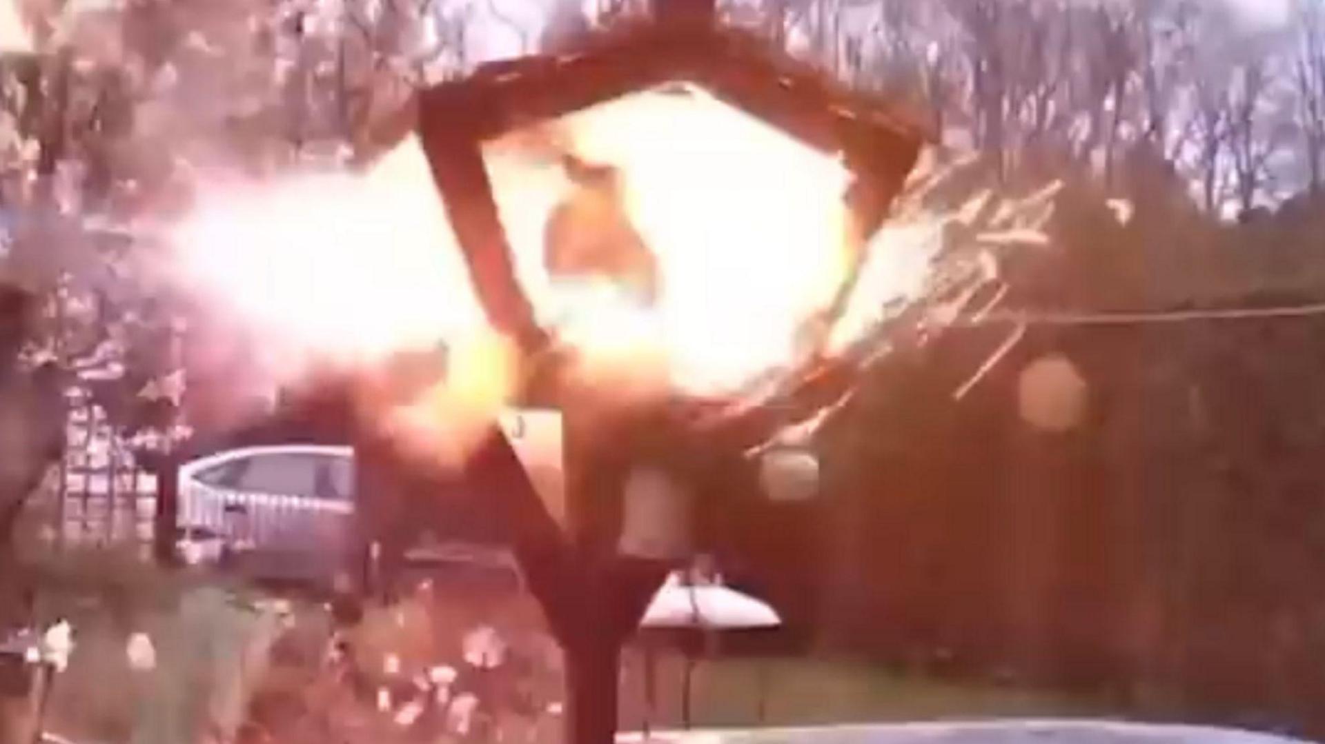 A triangular wooden bird table is engulfed by an orange flash. Sparks appear to be flying off the bird table. A cat is seen surrounded by the orange flash.