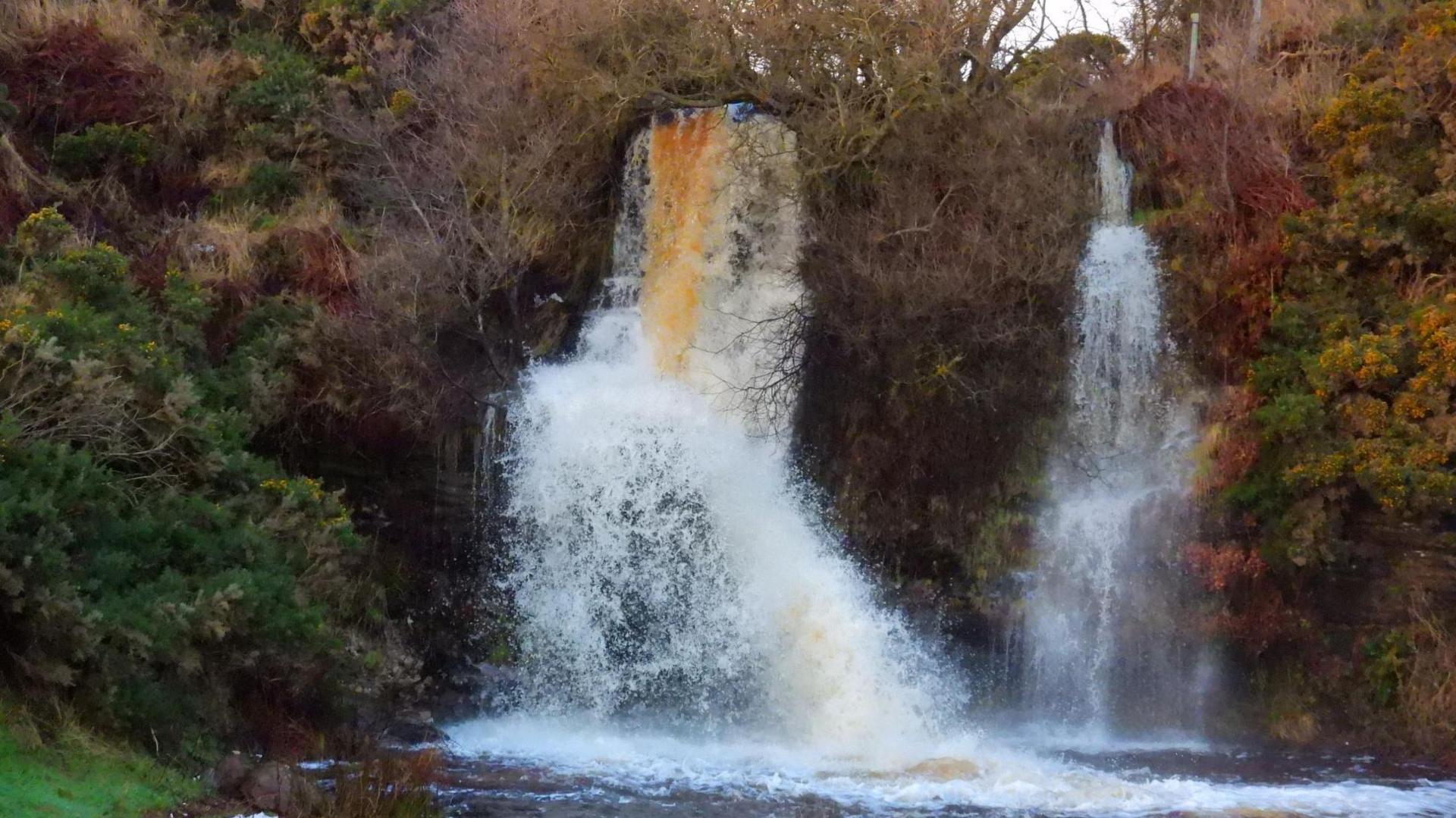 The waterfall is in full flow. There are sprays of white water where it hits rocks.