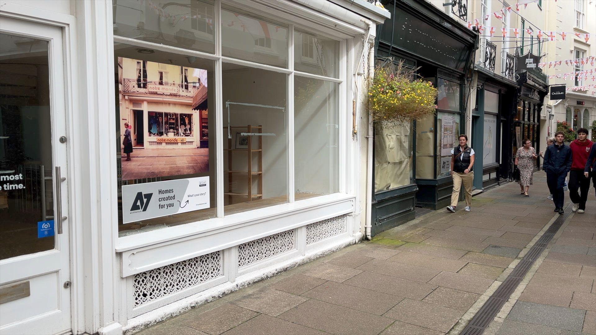 Empty shop fronts in Mill Street, St Peter Port, Guernsey. People can be seen walking on the right side of the image while a white empty shop is on the left with a boarded up green shop front next to it