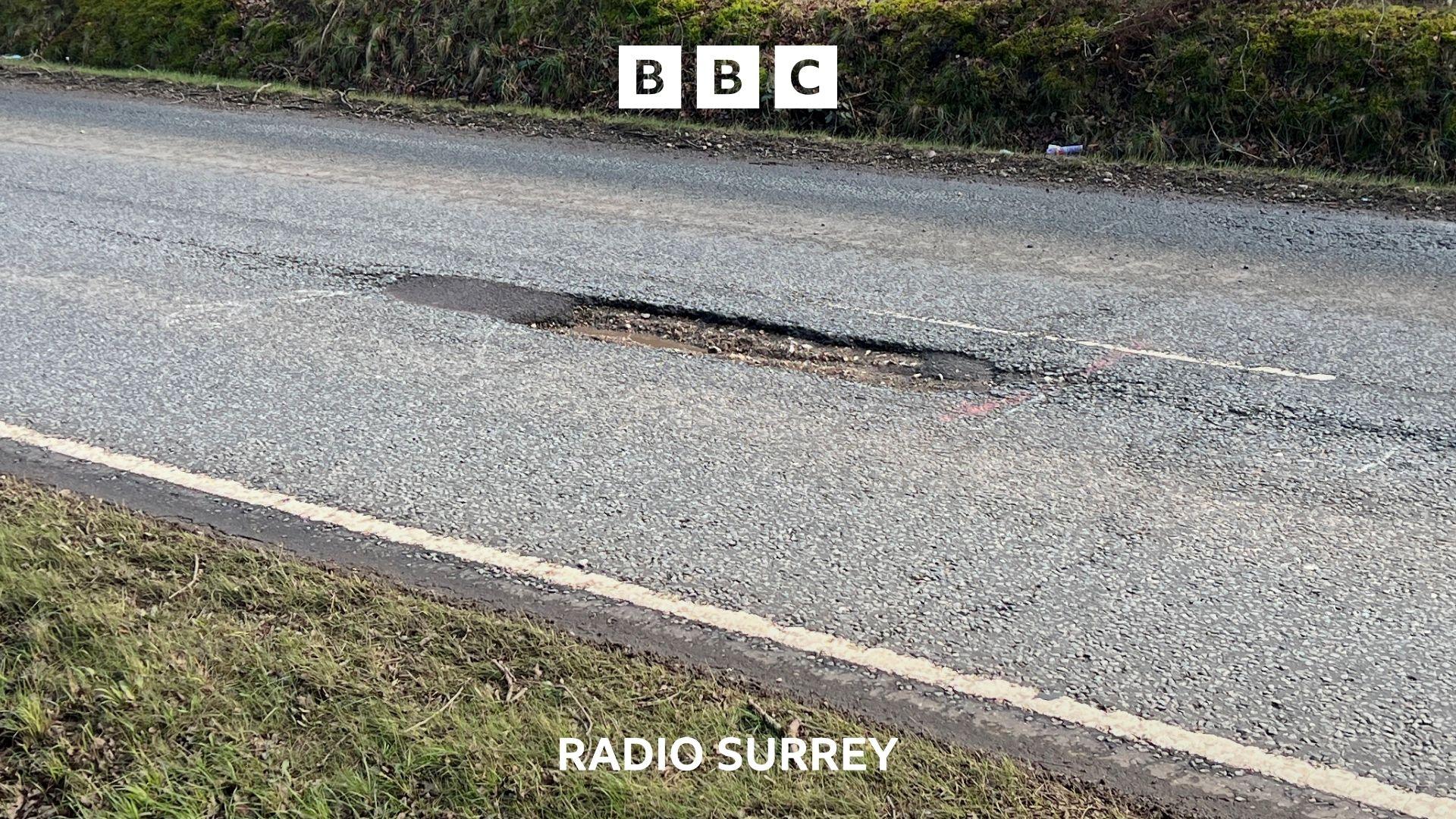 A stretch of single carriageway road with a large pothole in the centre.