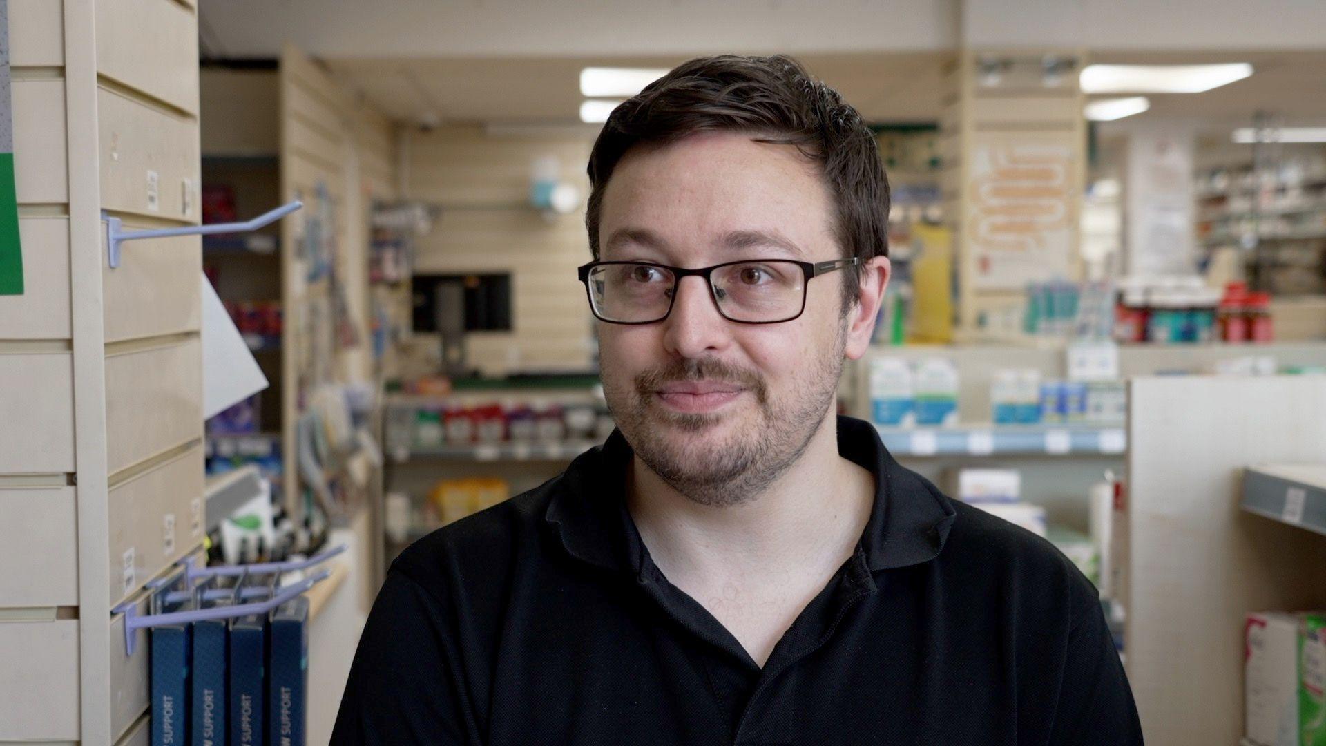 Mark Jackson in a dark shirt and glasses standing in his pharmacy