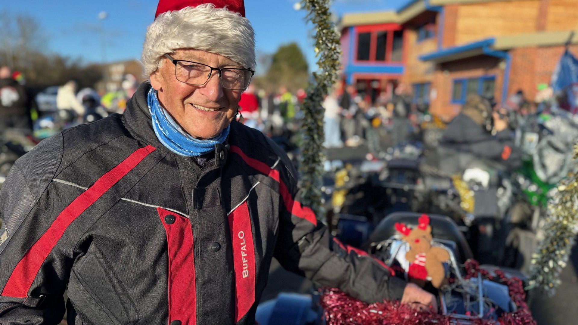 The event organiser John Judson is wearing a Santa hat and standing next to a motorbike decked with tinsel
