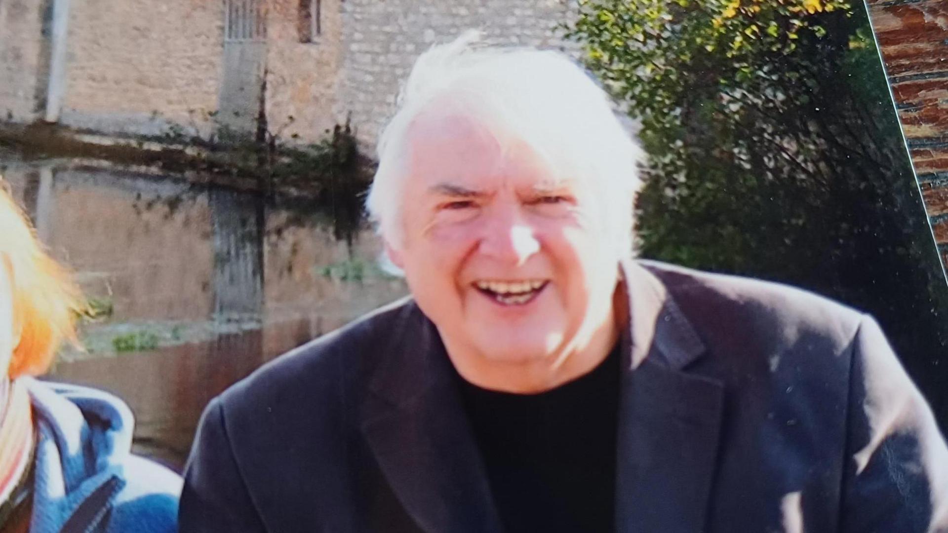 Jim Waters wearing a black suit and black t-shirt. He looks younger and is smiling