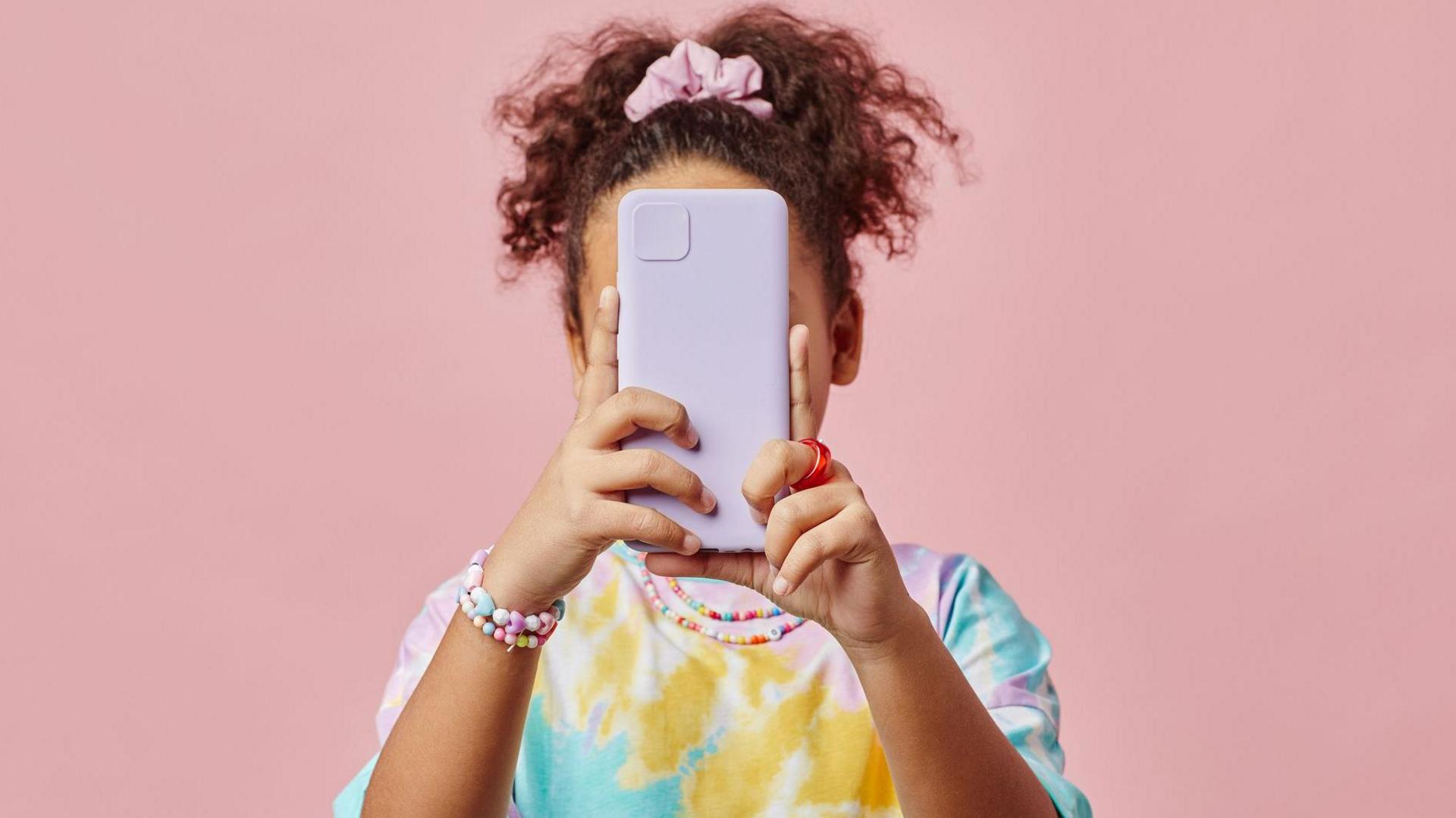 girl in a colourful t-shirt, with their phone covering their face