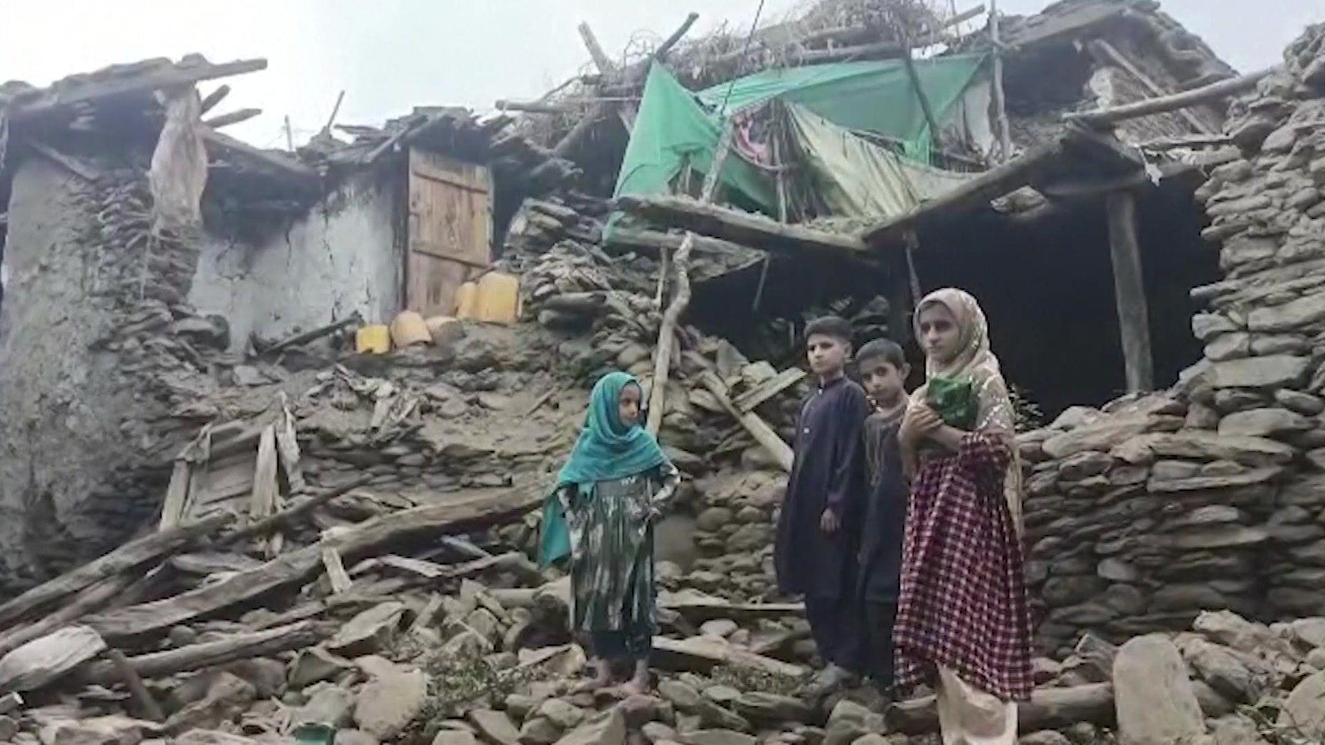A group of children stand in front of the rubble of a building