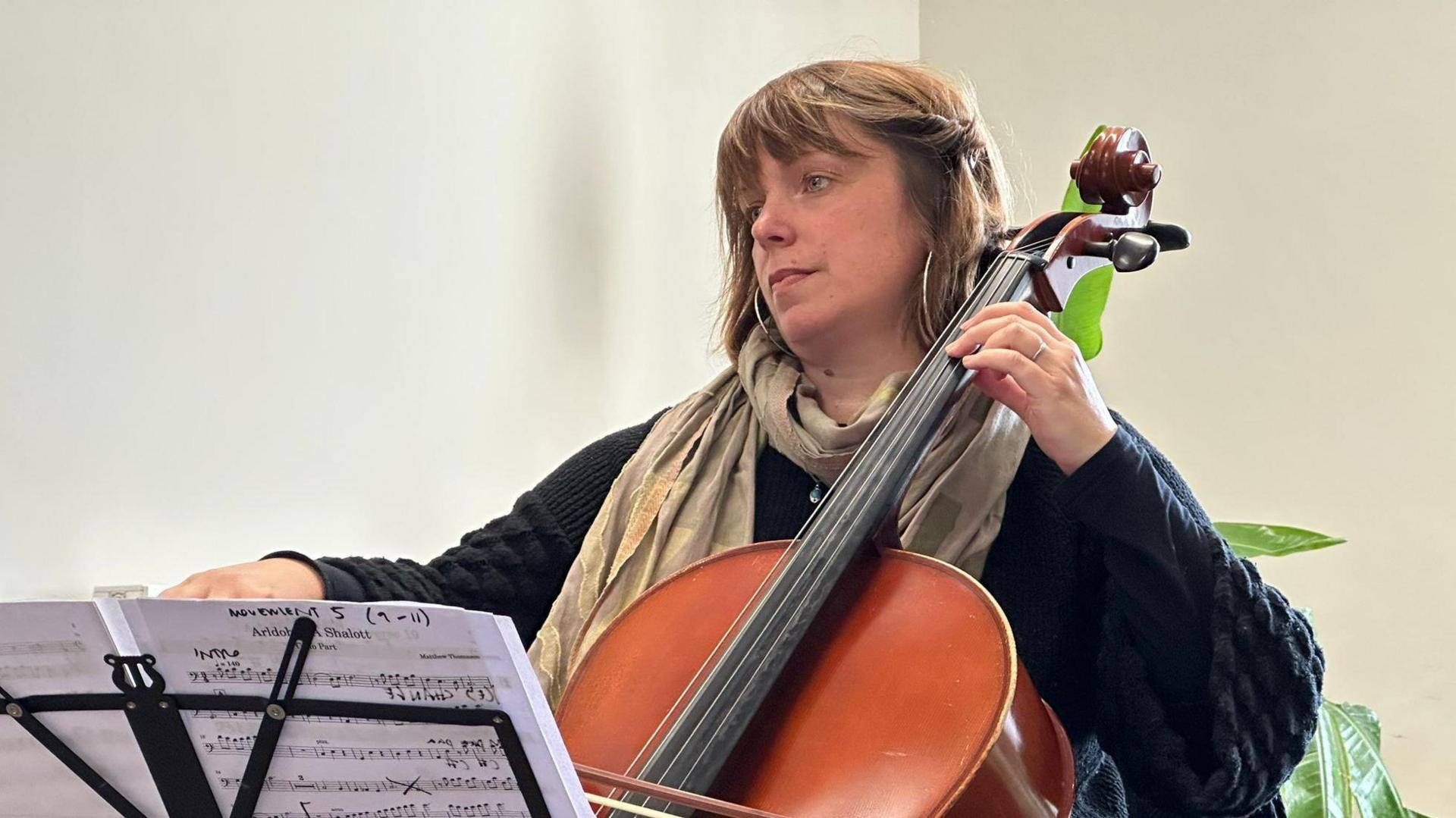 Kath playing cello in her hand with sheet music in front.