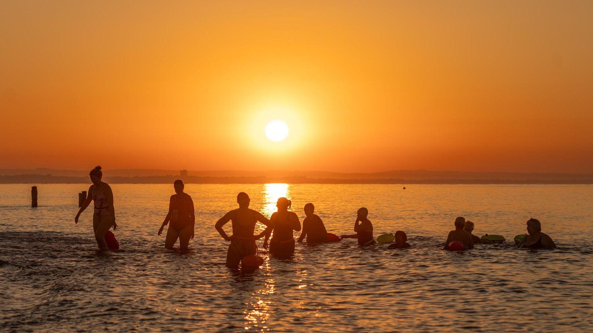 Swimmers in the sea with an orange sky and sun shining in the background