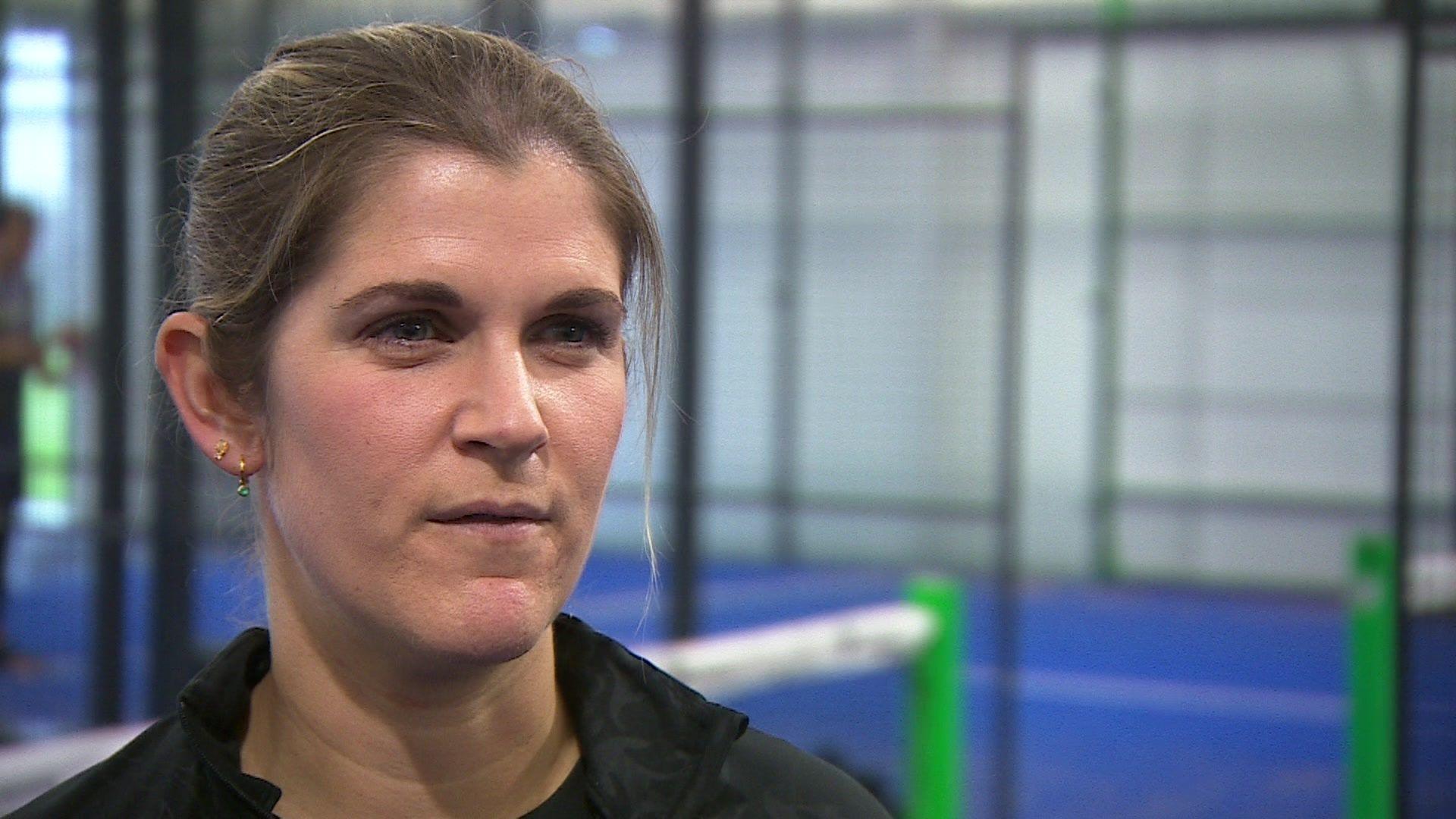 A head-and-shoulders picture of Becky Davis, wearing in a black top, standing in front of a net on a blue padel court