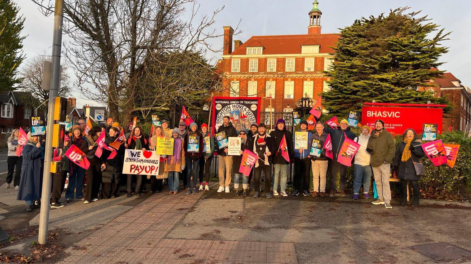 Dozens of teachers stage a protest outside a red brick school building. 