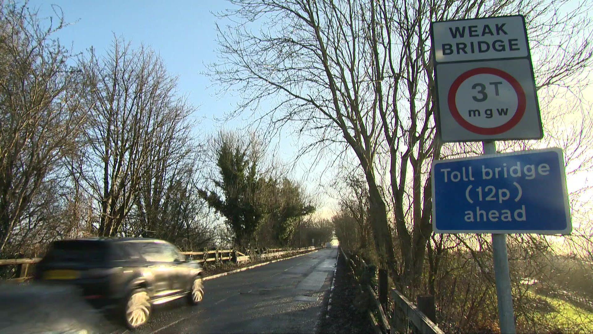 A view of a car going over the Warburton toll bridge, with a sign next to it saying toll bridge (12p) ahead