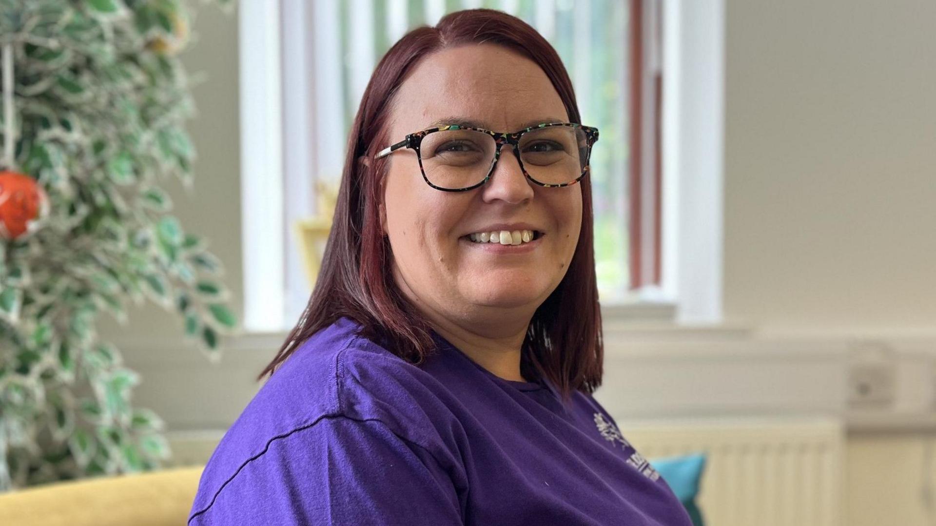 Woman in purple top and glasses smiling 