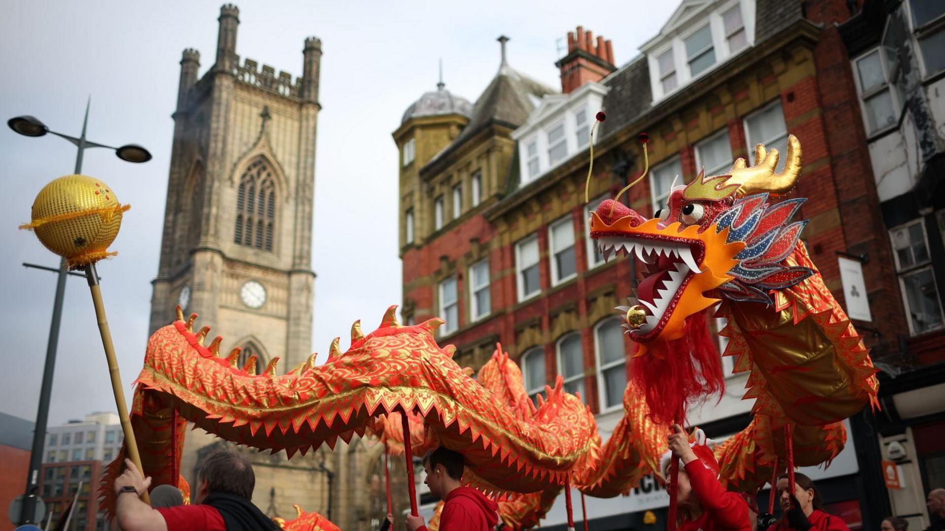 A red and gold dragon parades along Berry Street in Liverpool city centre with St Luke's church in the background.