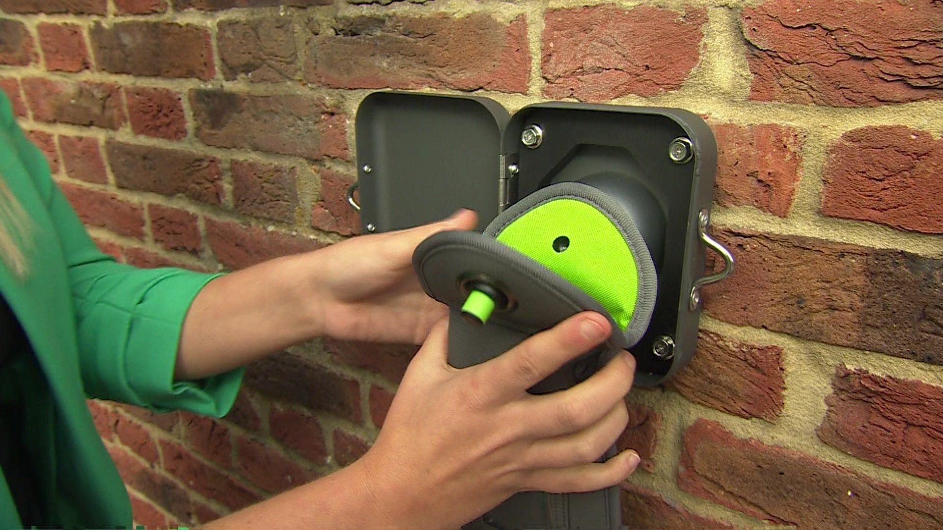 A grey and green phone pouch being held against a square plastic unlocking device attached to a brick wall