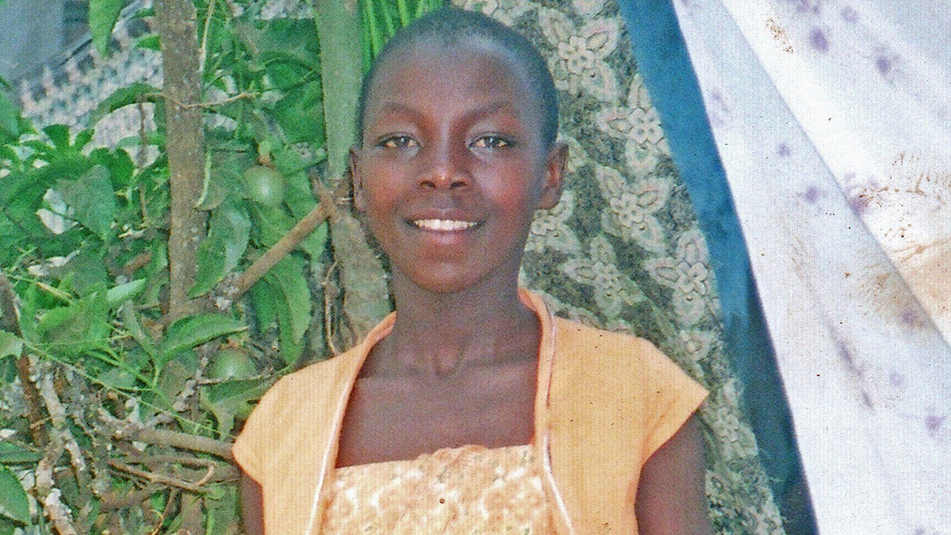 Monic smiles at the camera - she is wearing a yellow and white lace dress with a yellow shirt over the top