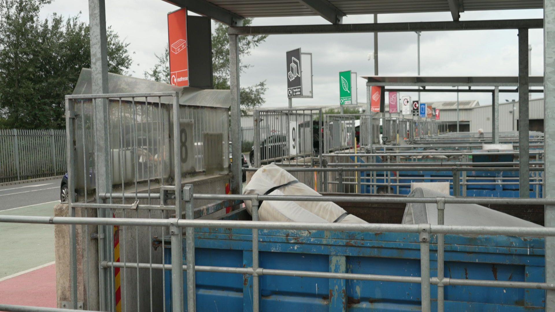 Rows of recycling bays at the Bredbury centre in Greater Manchester. Waste can be seen coming out of blue containers, with colourful signs marking the different types of recycling that can be accepted. 