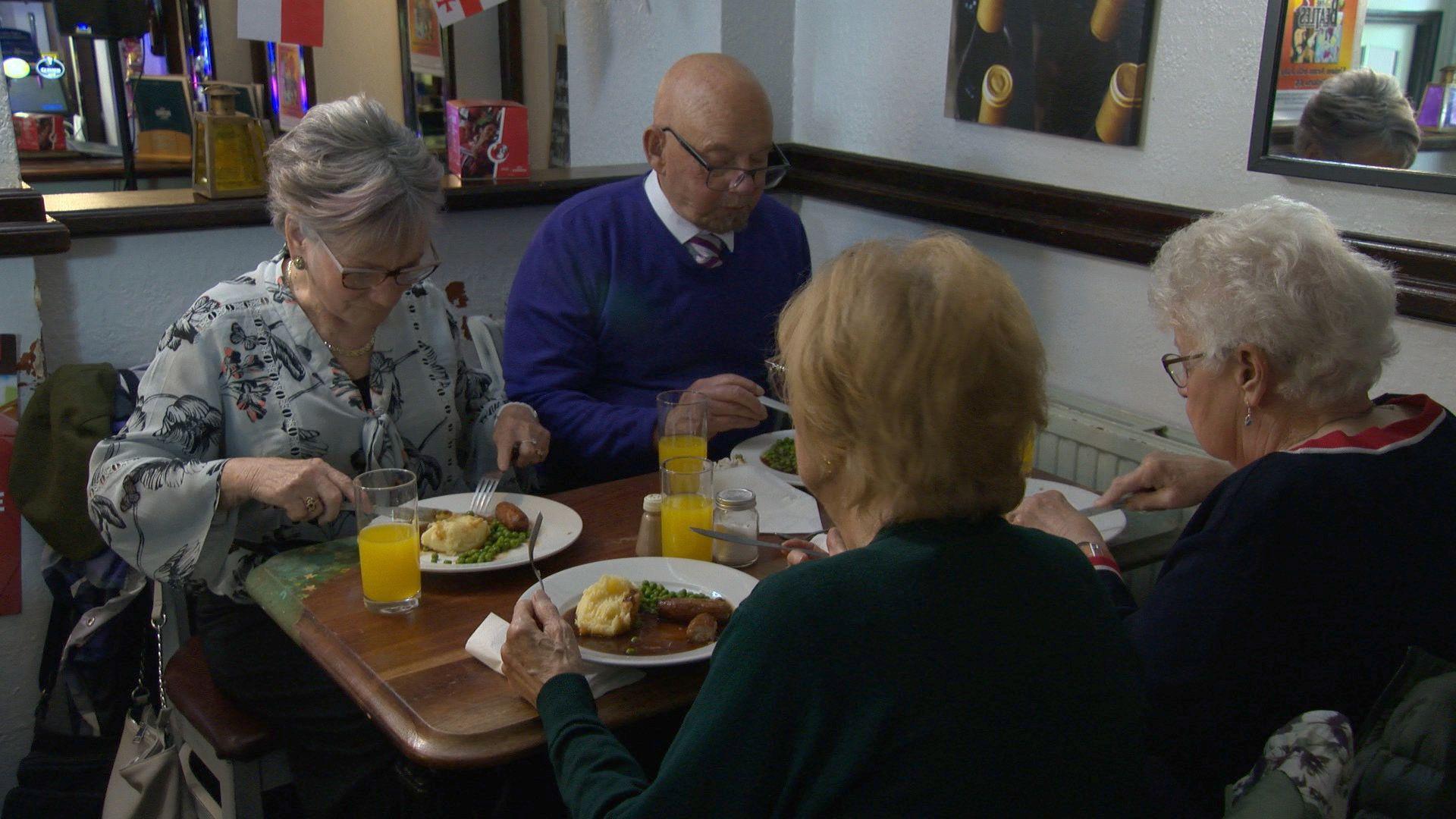 Three women and a man eating a meal in a pub