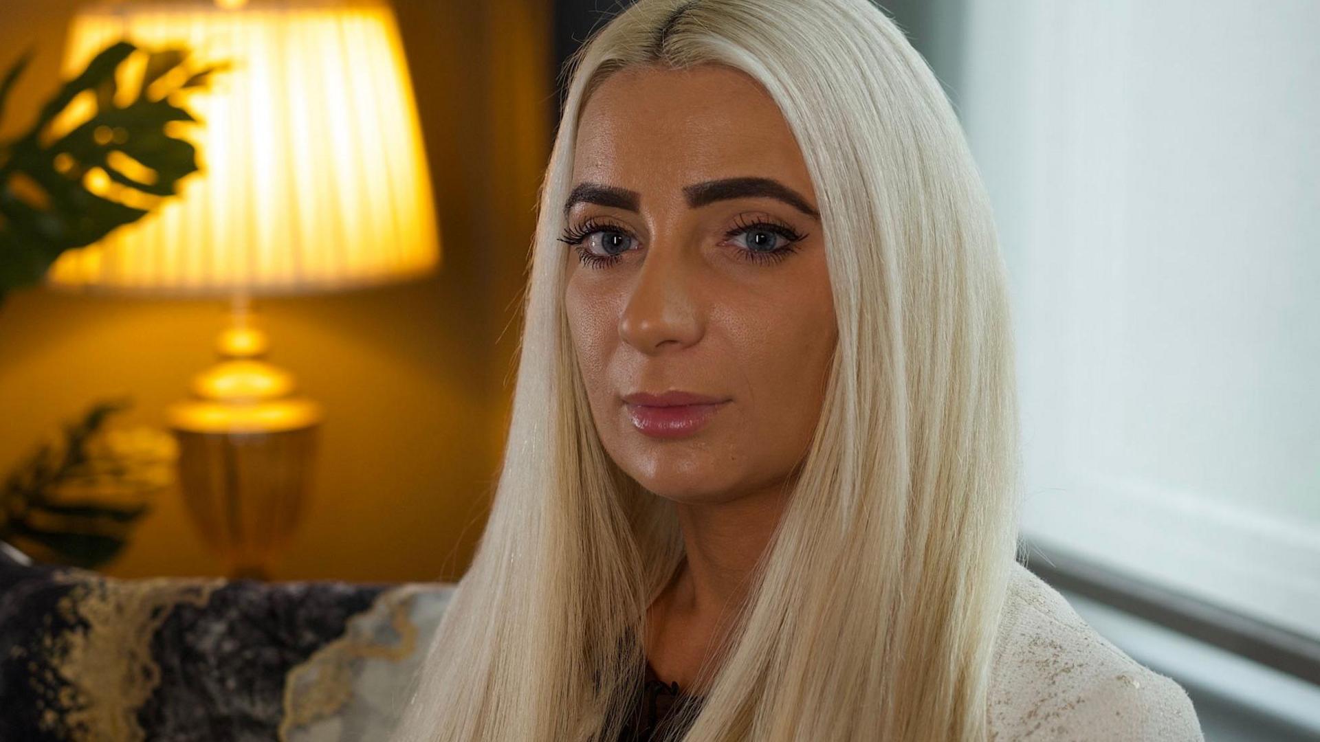 Charlotte Smith has long, white blonde hair and is wearing a white jacket. She is sitting in front of a window and looking at the camera.