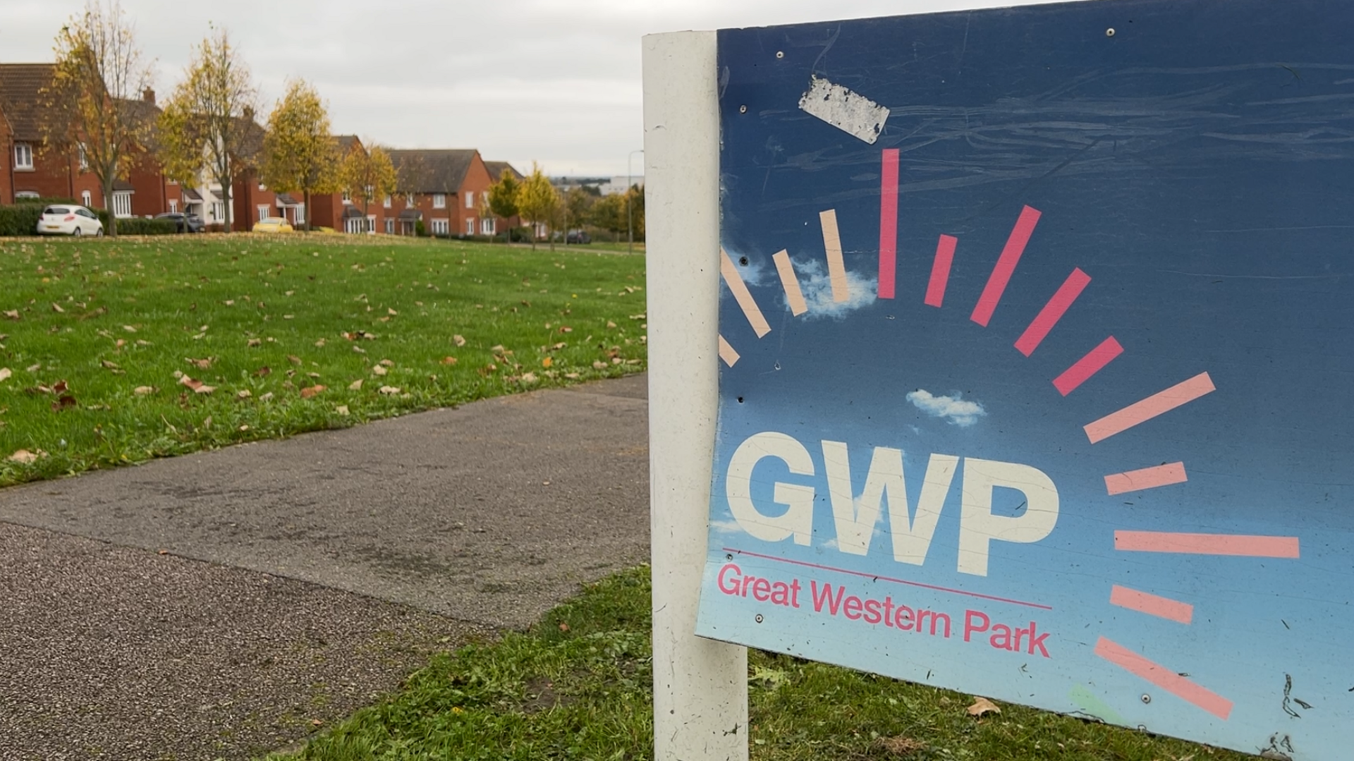 A blue sign saying "GWP" with "Great Western Park" underneath it. In the background is a green area with houses in the distance. 