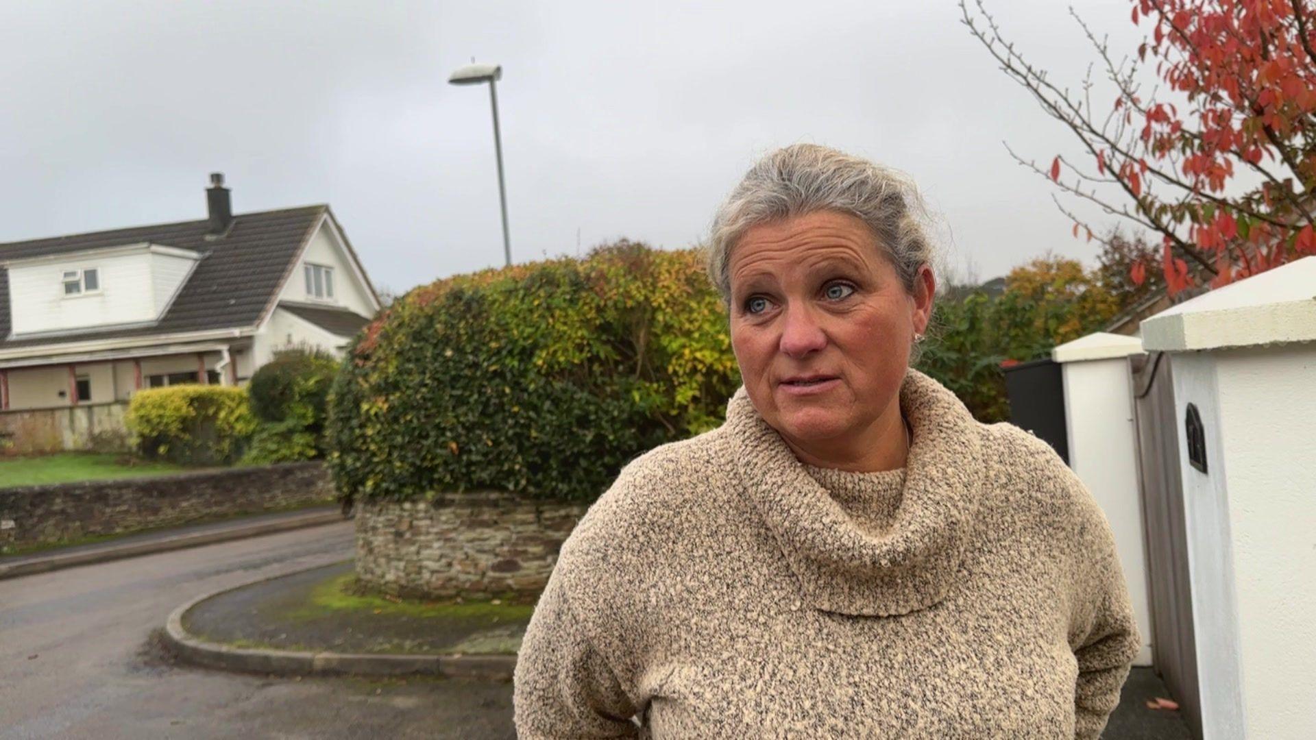 A woman with a beige jumper looking away from the camera in a residential setting.