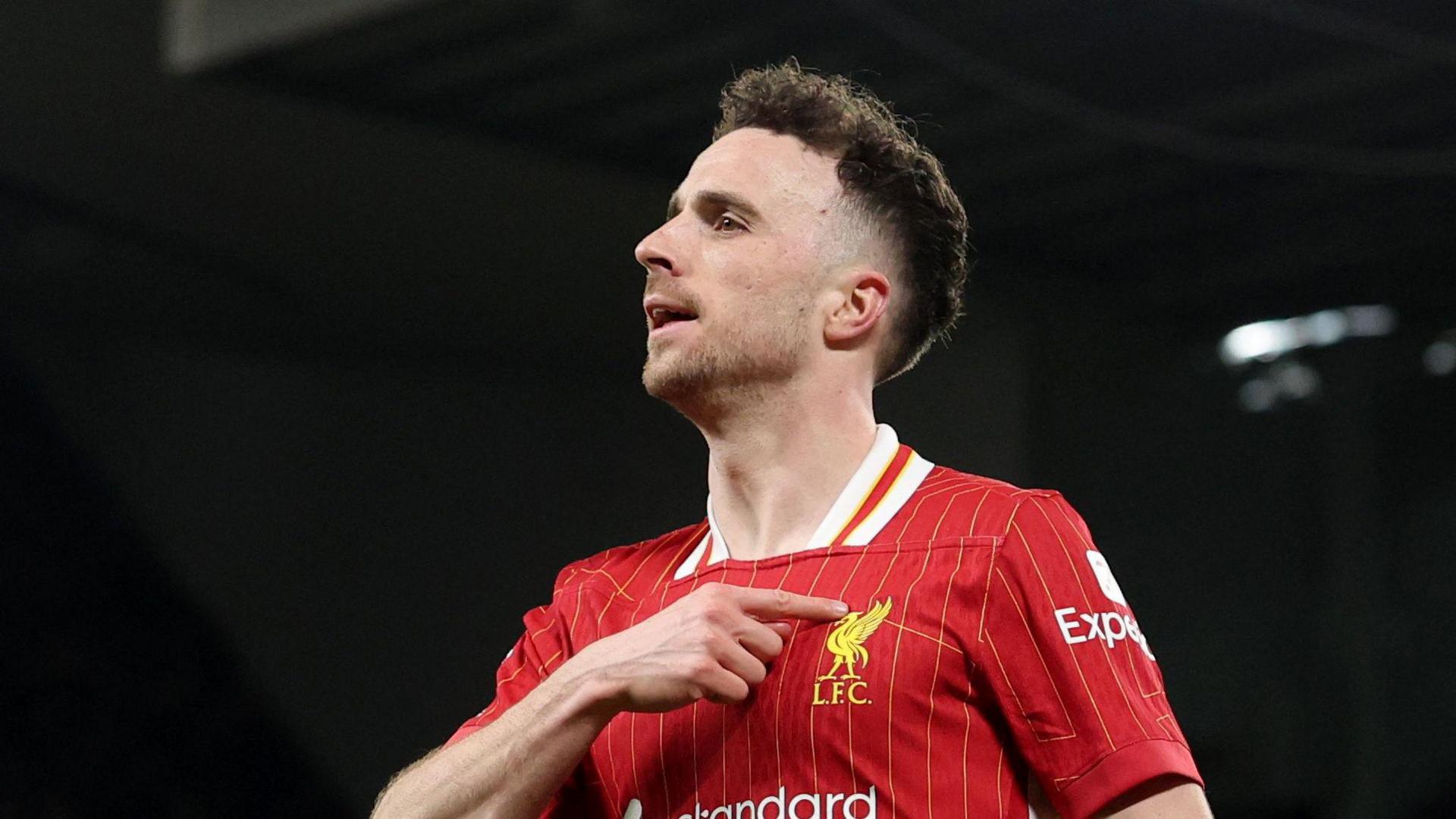 Jota pointing to the Liverpool badge on his shirt.