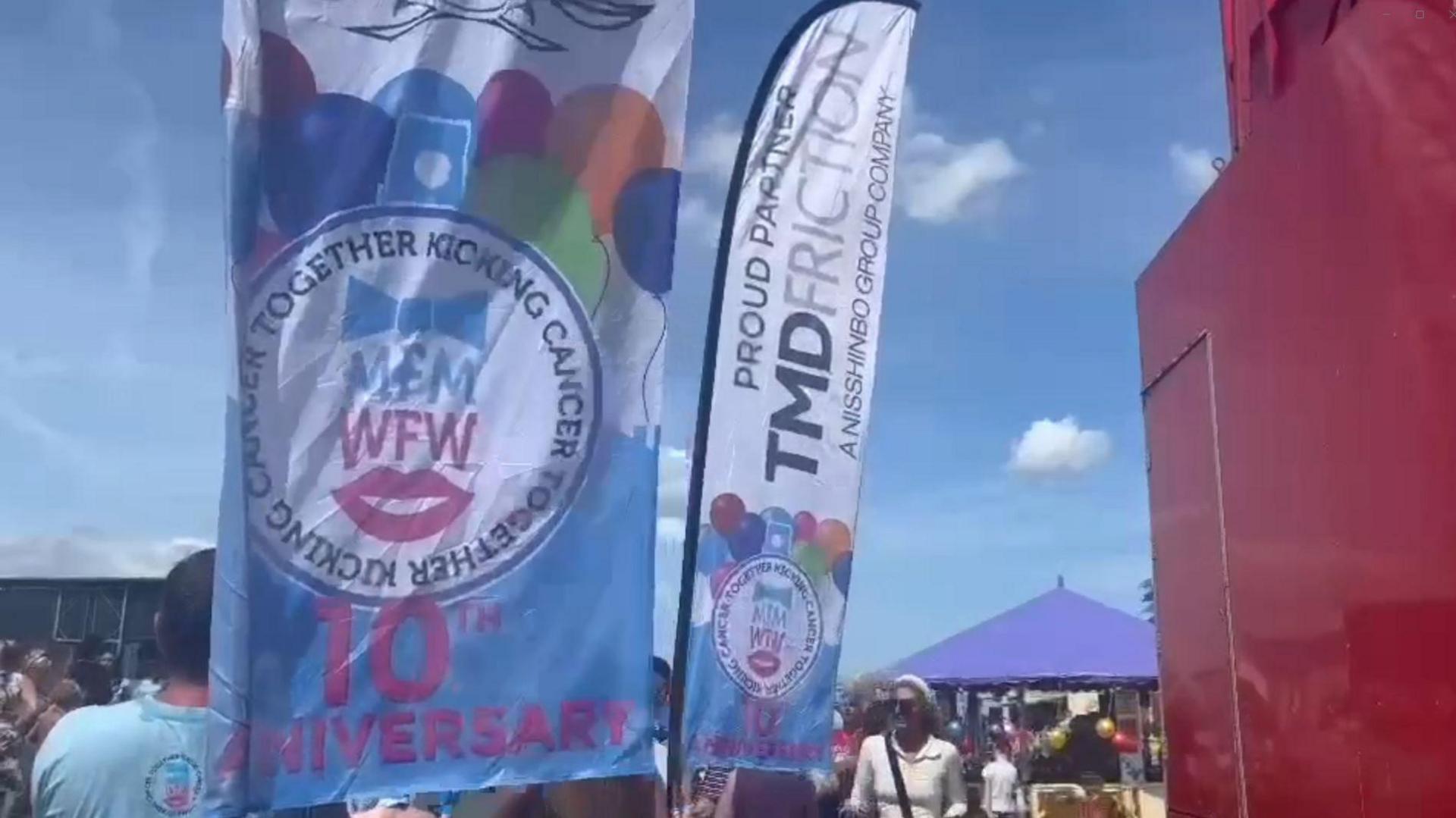 Dozens of people in a crowd at the charity fun run. Banners show that it is the 10th anniversary of the run.