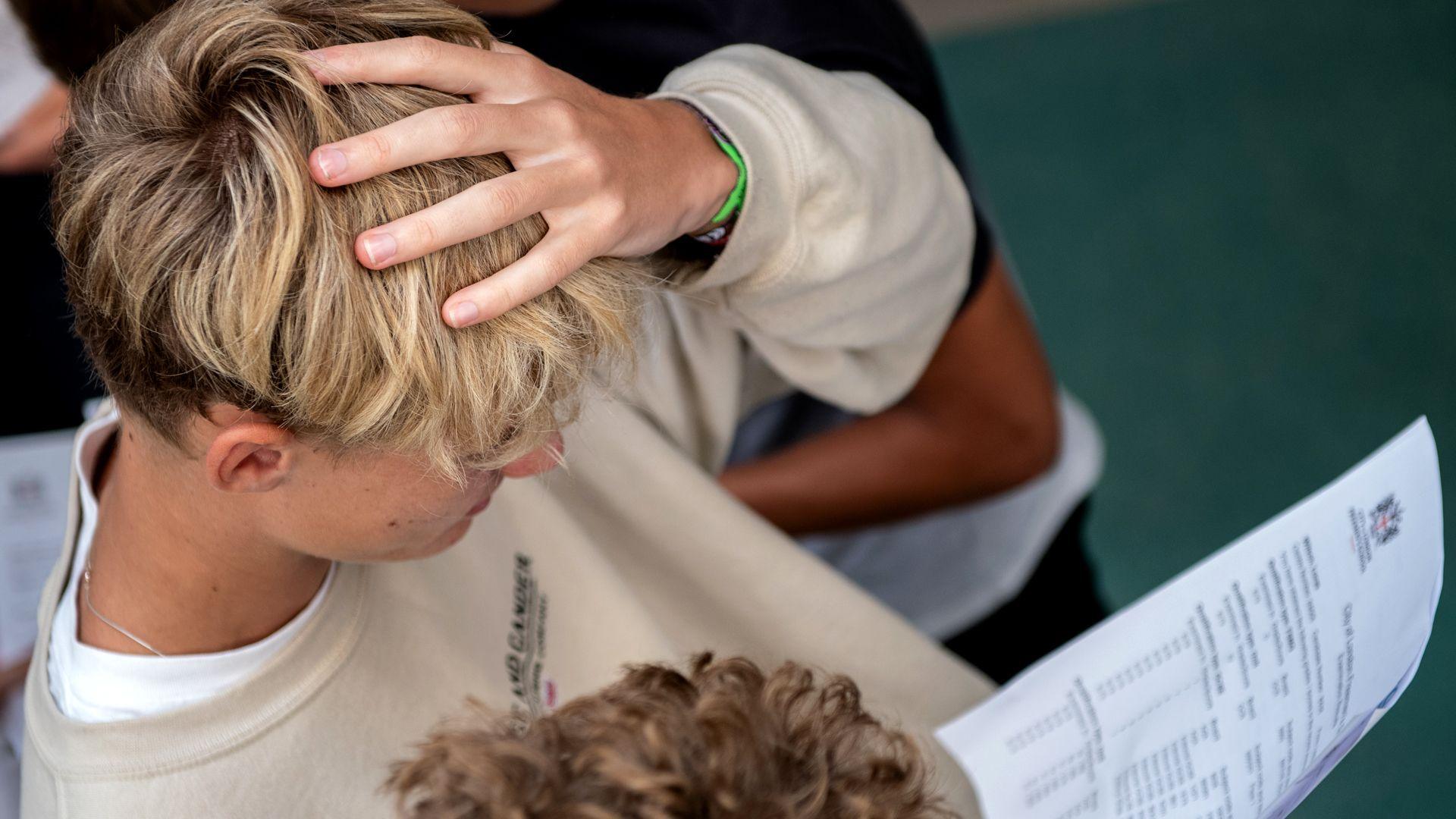 A student with blonde hair holds their hand to their head as they look at their GCSE results at the City of London Freemen's School