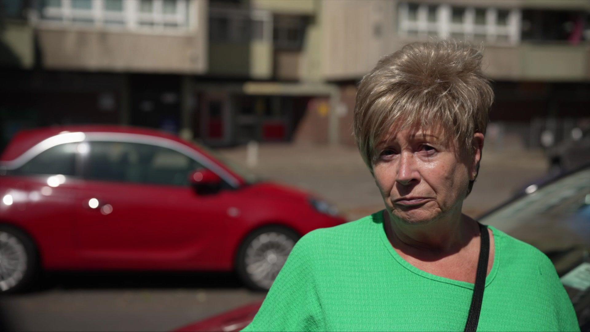 Sandra wearing a green top and stood in front of two cars