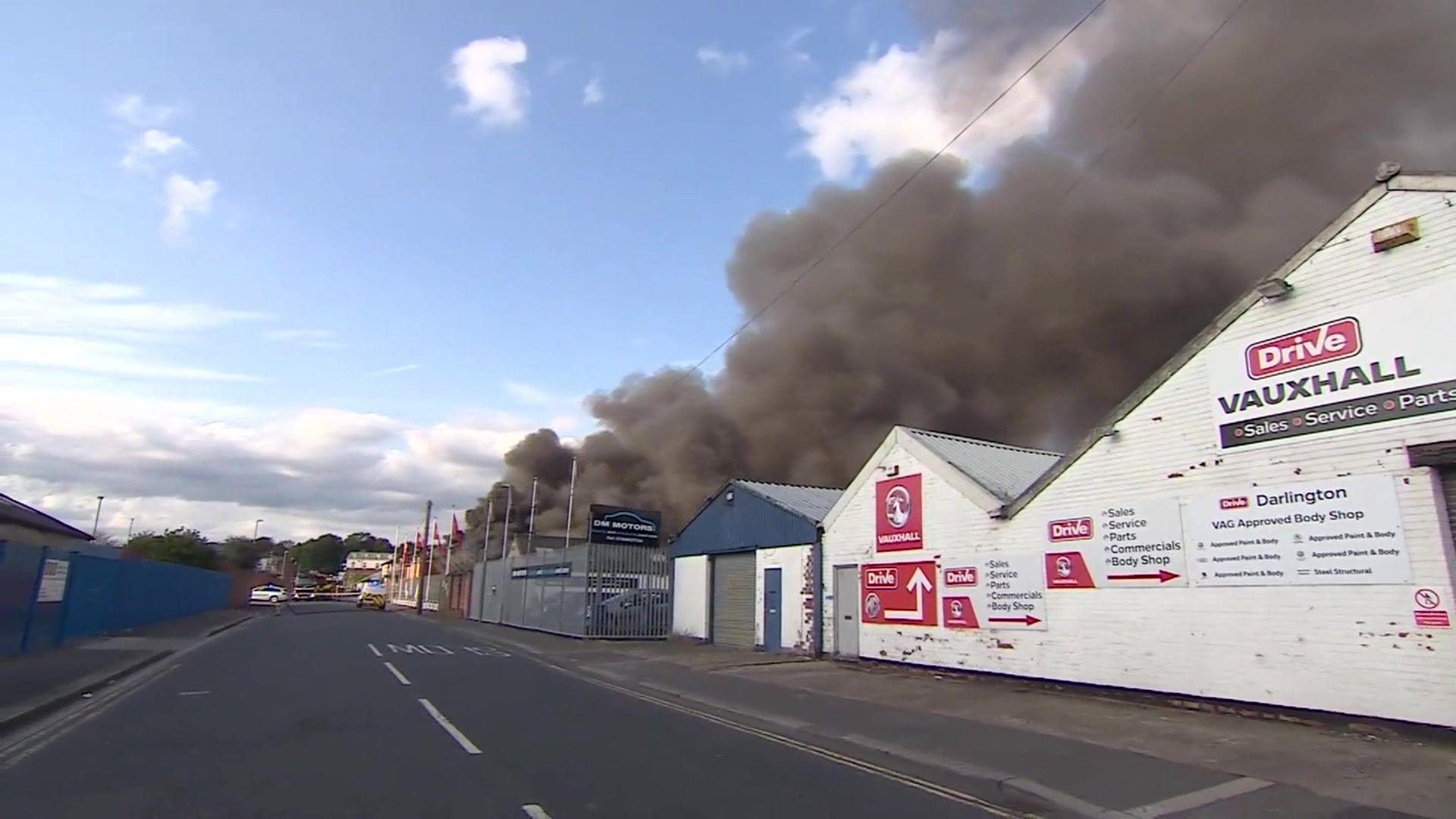 A dark cloud of smoke has blown over several industrial buildings.