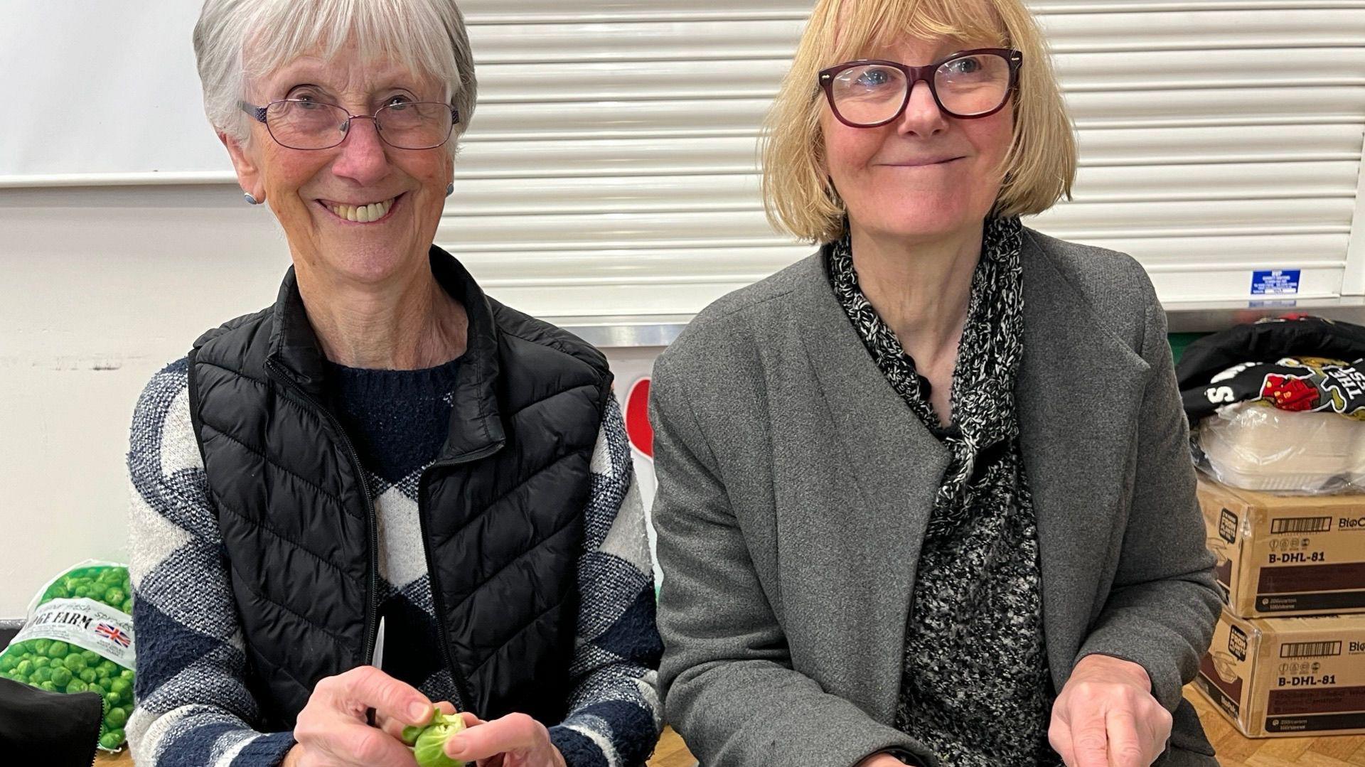 A smiling mother and daughter peel sprouts.