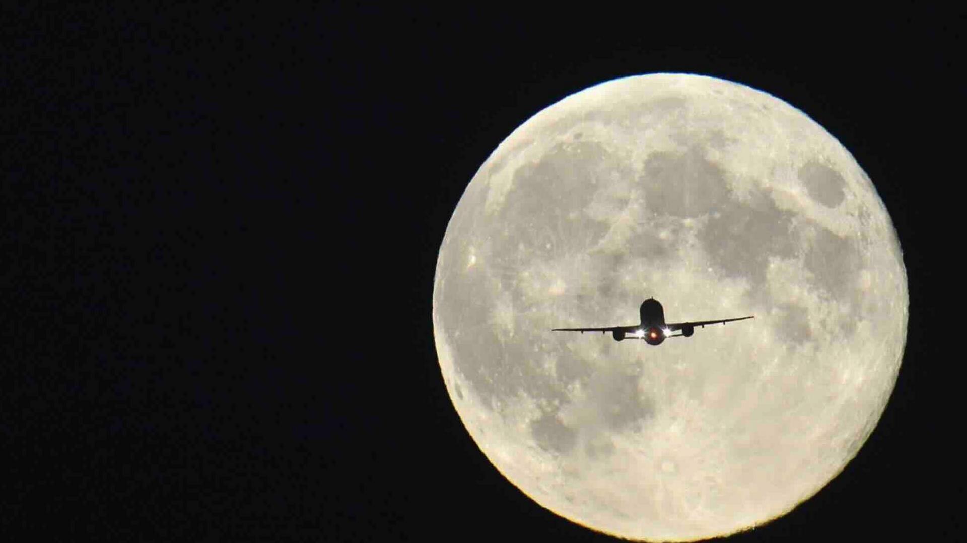 A plane is silhouetted by a full Moon and a dark black night sky