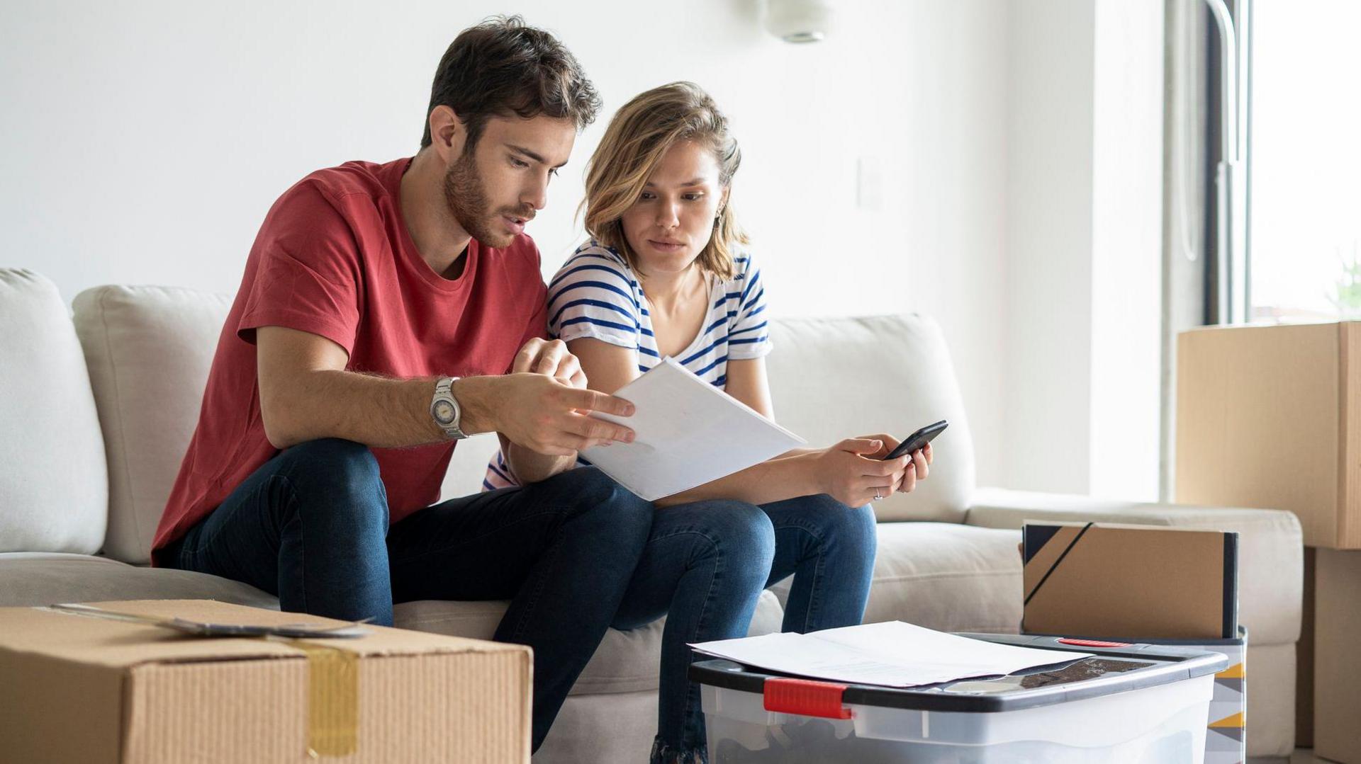 Young couple sat in a living room surrounded by cardboard boxes