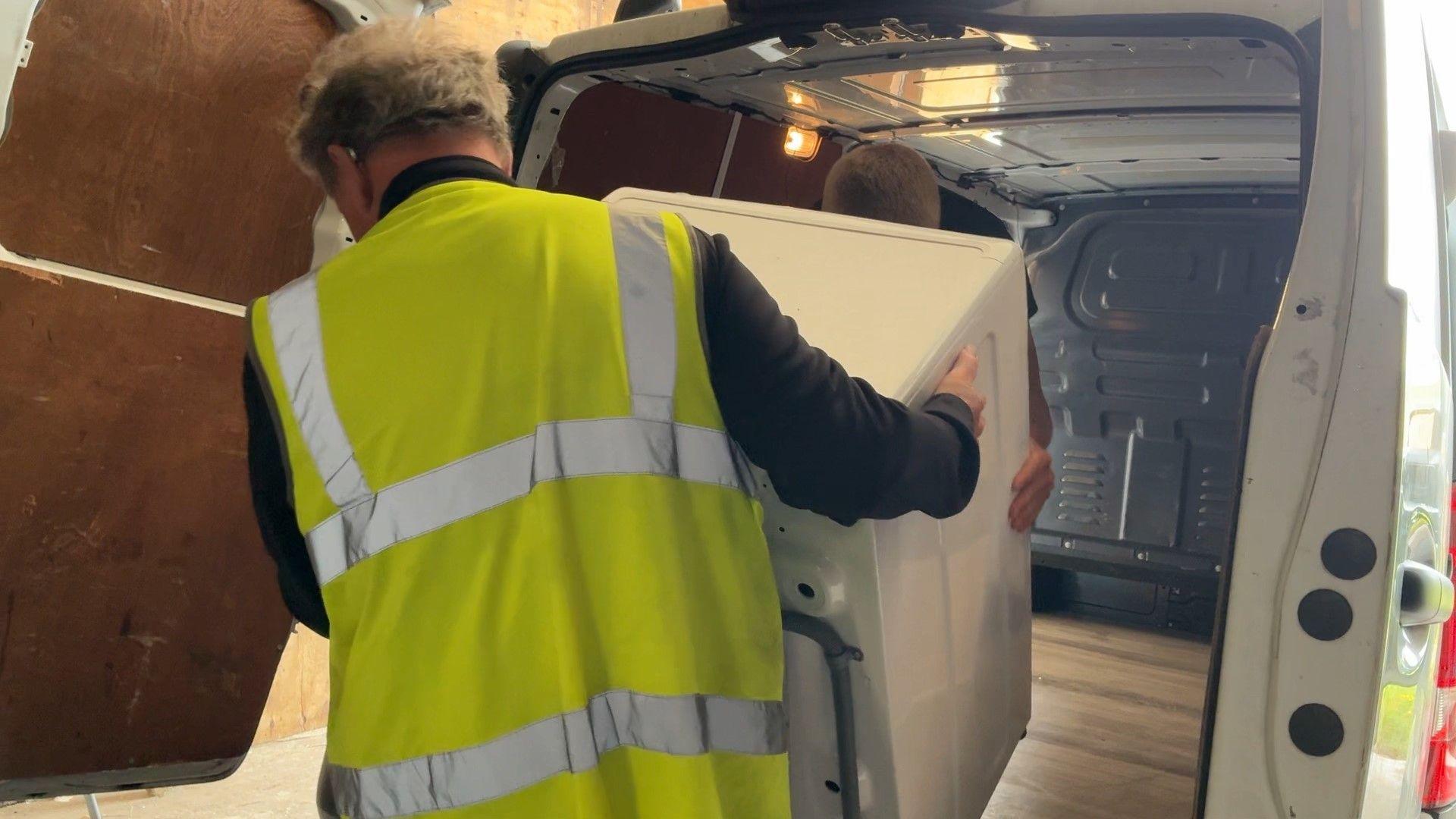 Image of two men putting a fridge into a van