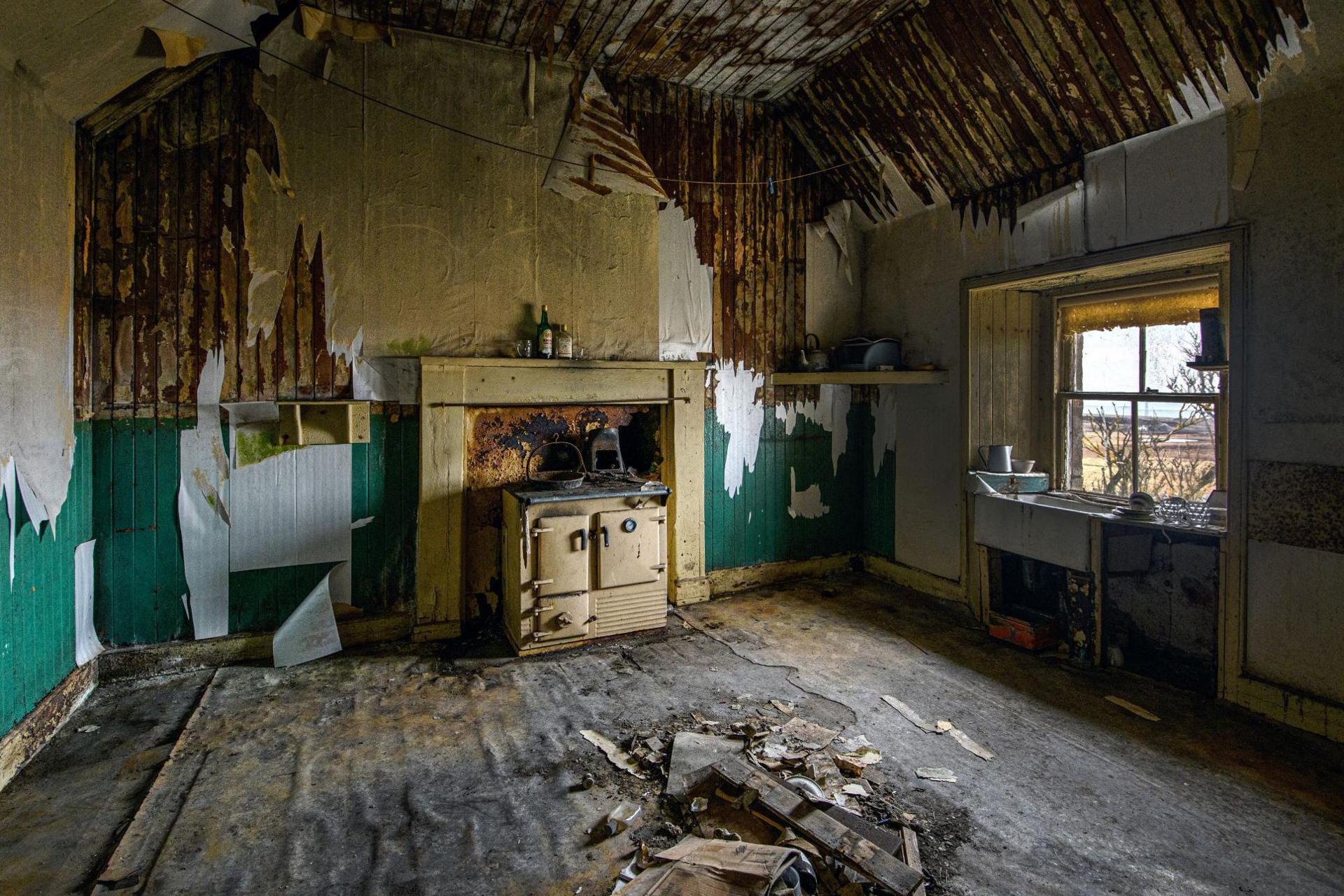 The room has wall paper stripped from the walls. There is a pile of debris on the floor and an Aga-style cooker on the gable end wall.