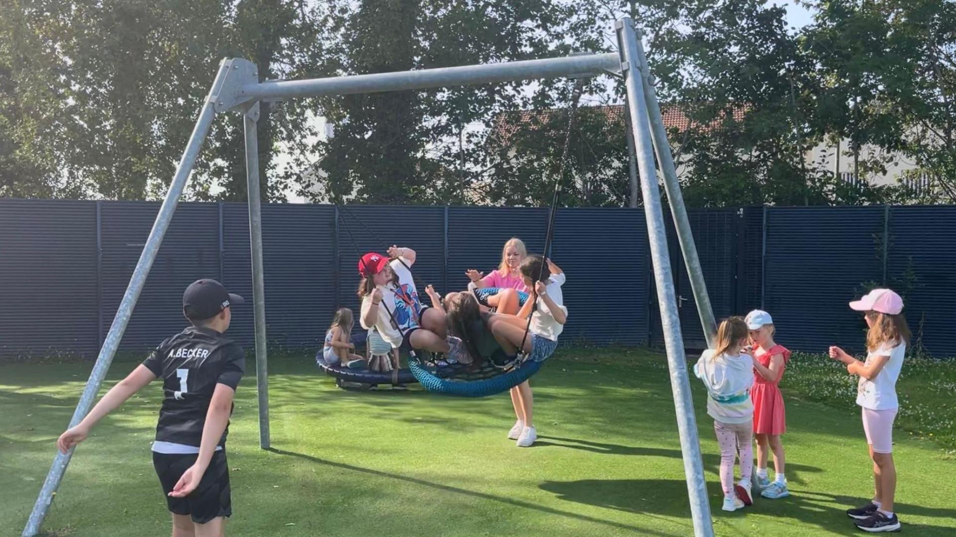 A number of children on a hammock swing in a park in the sunshine