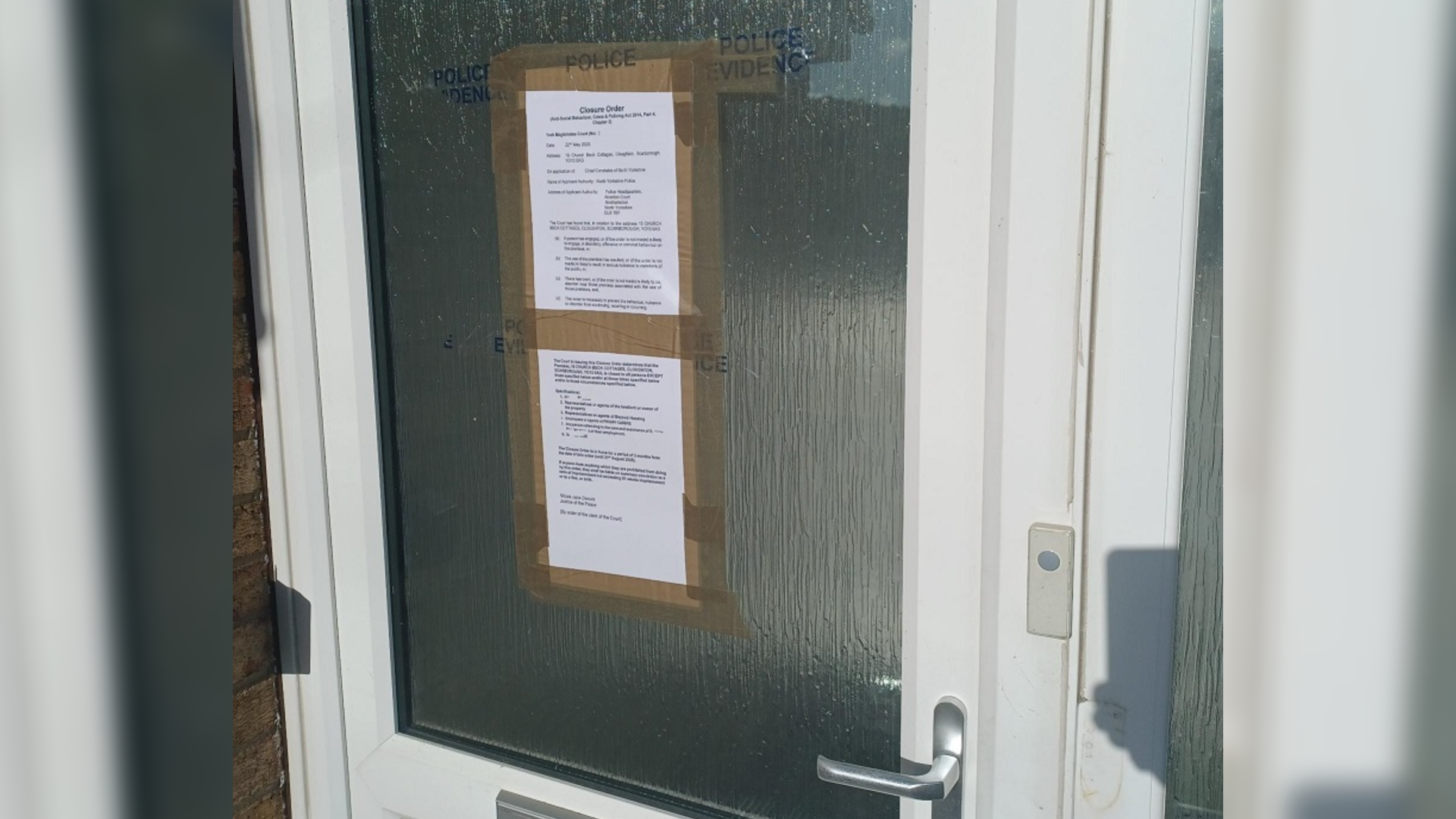 A front door with two sheets of paper taped to it, alongside blue lettering saying "police evidence".