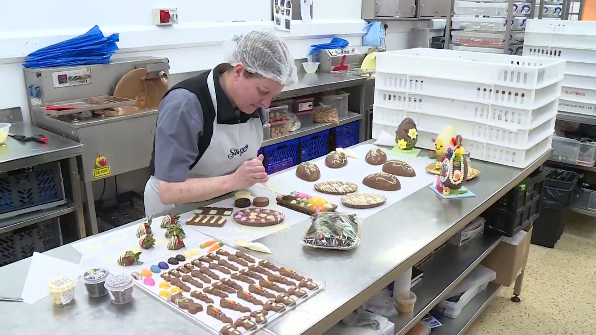 A chocolatier piping cream onto chocolate products on a large steel table.